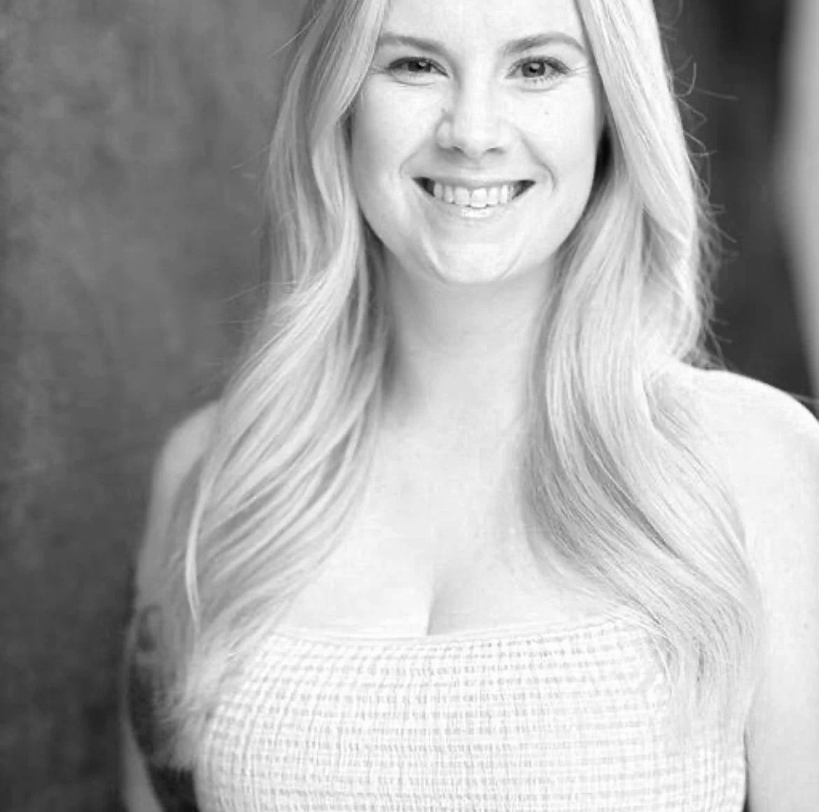 Leah is a white woman with long, straight blonde hair, she is wearing a checker printed tank top and smiling.