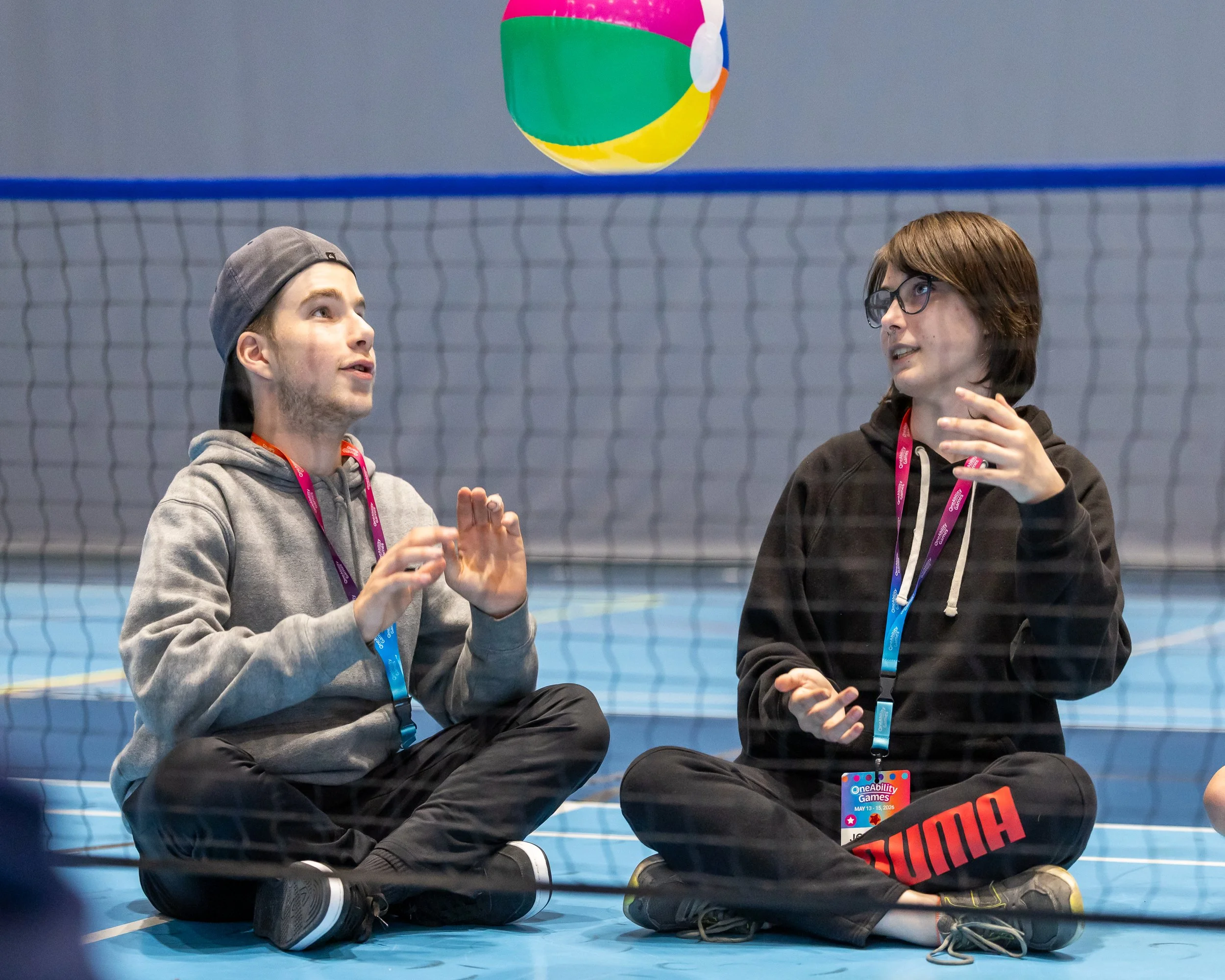 Two youth sitting on a volleyball court playing sitting volleyball with an incoming beach ball