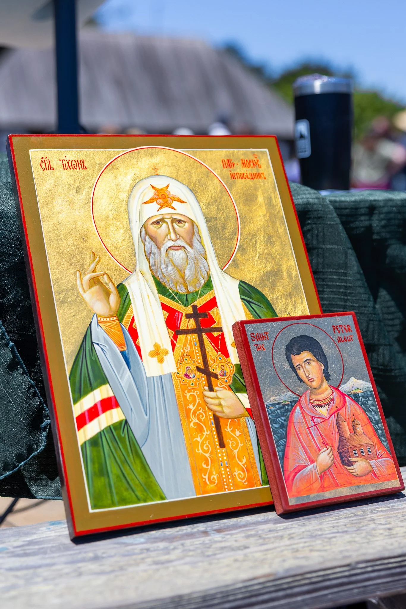 Two religious icons, one large and one small, featuring saints with halos, depicted in traditional iconographic style, displayed outdoors on a wooden surface.