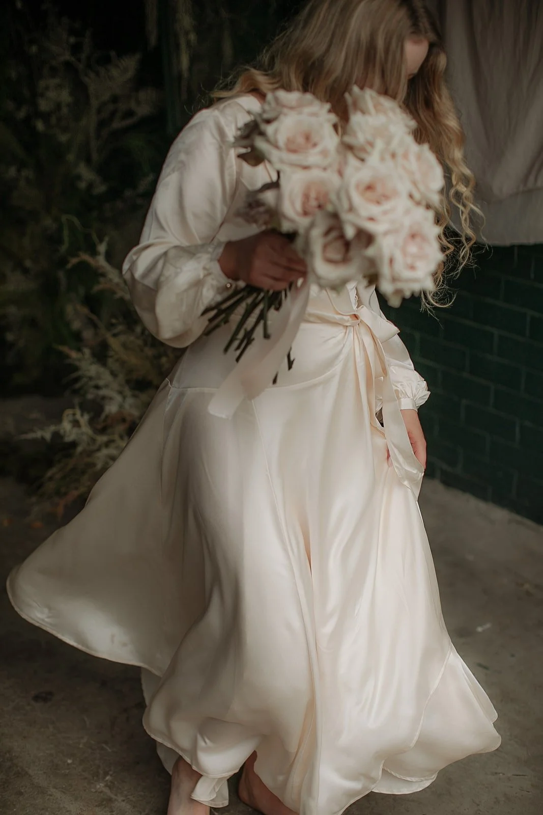 Woman in a white silk dress carrying a bouquet of blush pink roses