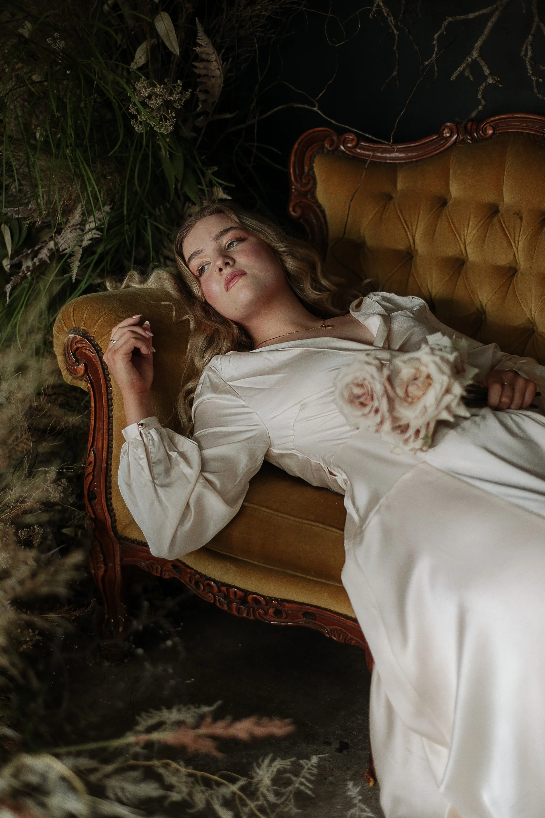 woman lying on a gold tufted couch with blush roses in her hand