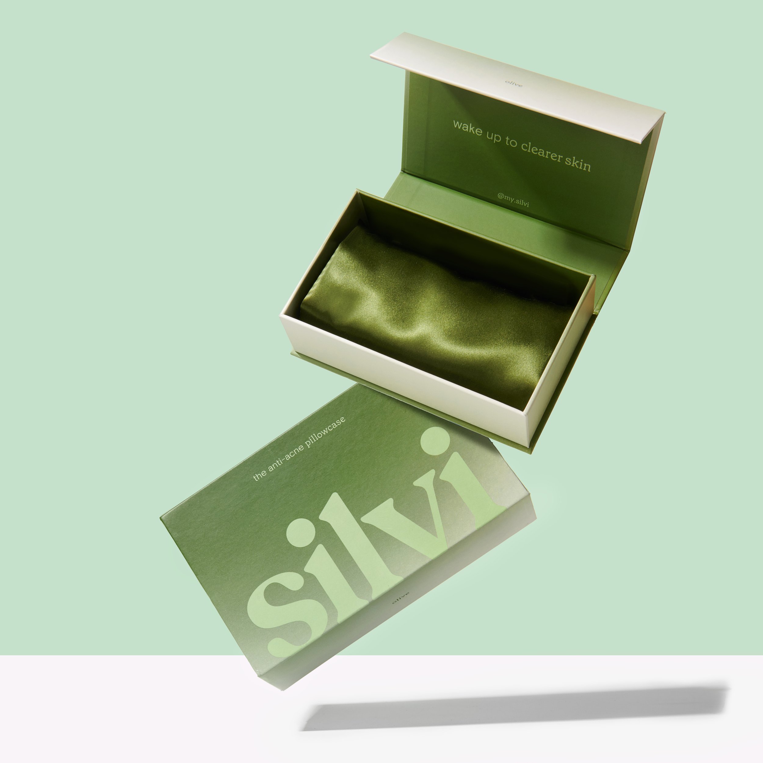 Silvi anti-acne pillowcase in packaging, green silk fabric visible inside opened box, displayed on light green background.