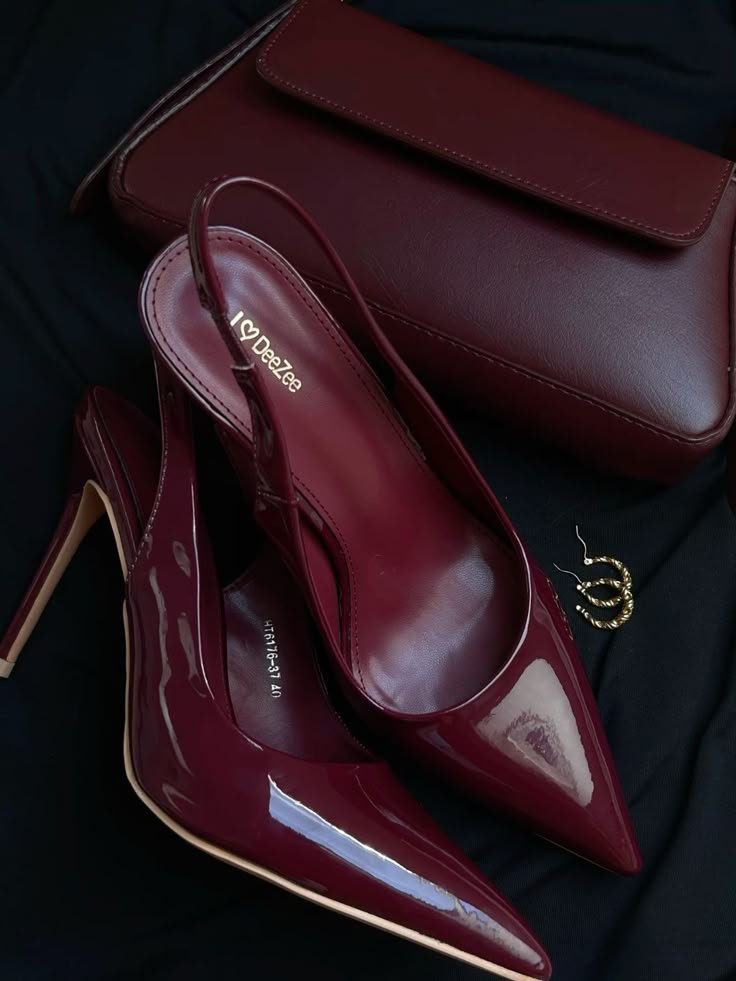 Maroon high heels with a matching handbag and gold hoop earrings on a dark fabric background.
