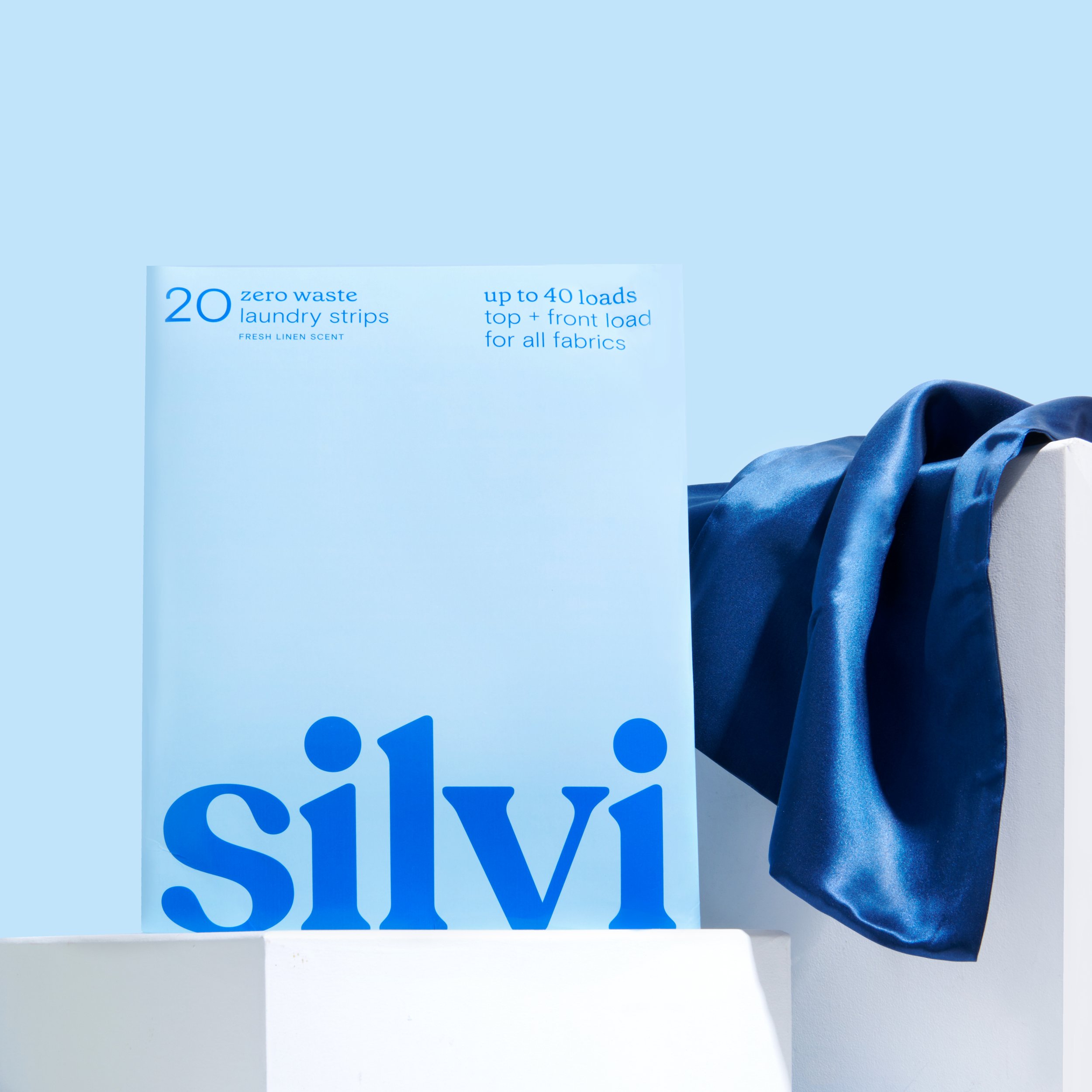 Blue packaging of Silvi zero waste laundry strips and a dark blue silk fabric on a light blue background.