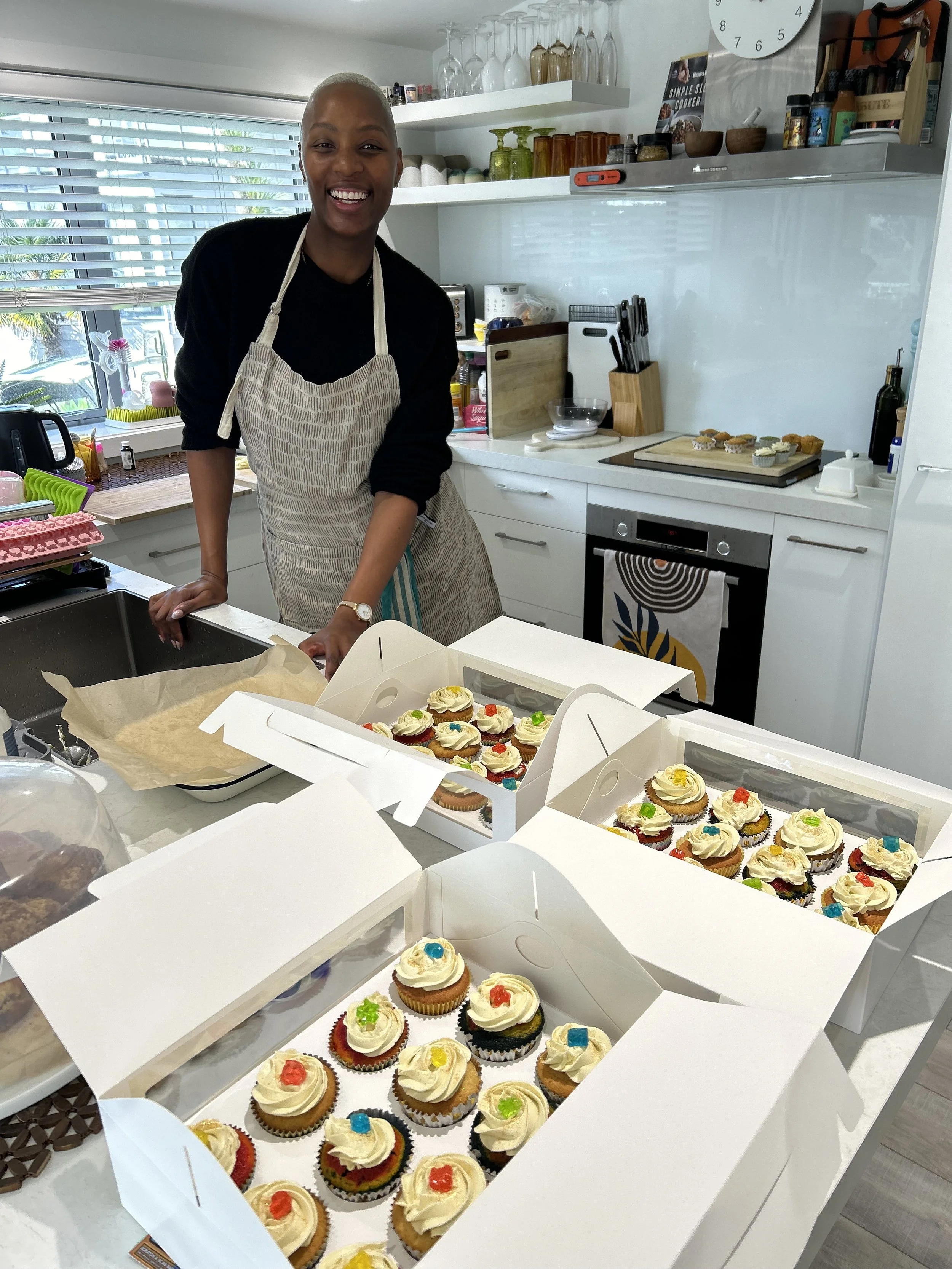 Mrs MacKay in the kitchen with her apron, standing with her recently decorated cupcakes with delicious toppings.