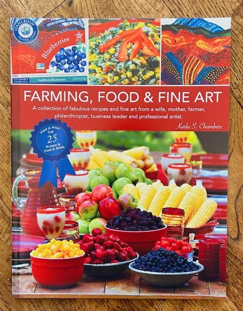 Book titled 'Farming, Food & Fine Art' featuring fruits, vegetables, jars of preserves, and small cups of pudding or yogurt on a table with a colorful cloth. The cover highlights 25 years of food and drink recipes from the author, Karla S. Chambers.