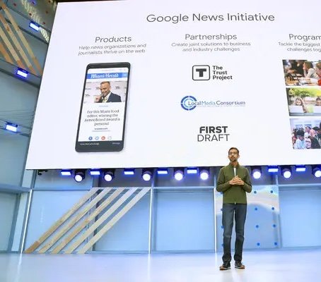 Sundar Pichai speaking on stage displaying details about the Google News Initiative.
