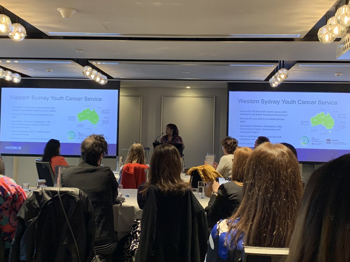 A presentation about Western Sydney Youth Cancer Service in a conference room, with a speaker at a podium and attendees seated at tables. The presentation slide discusses cancer services for young people.