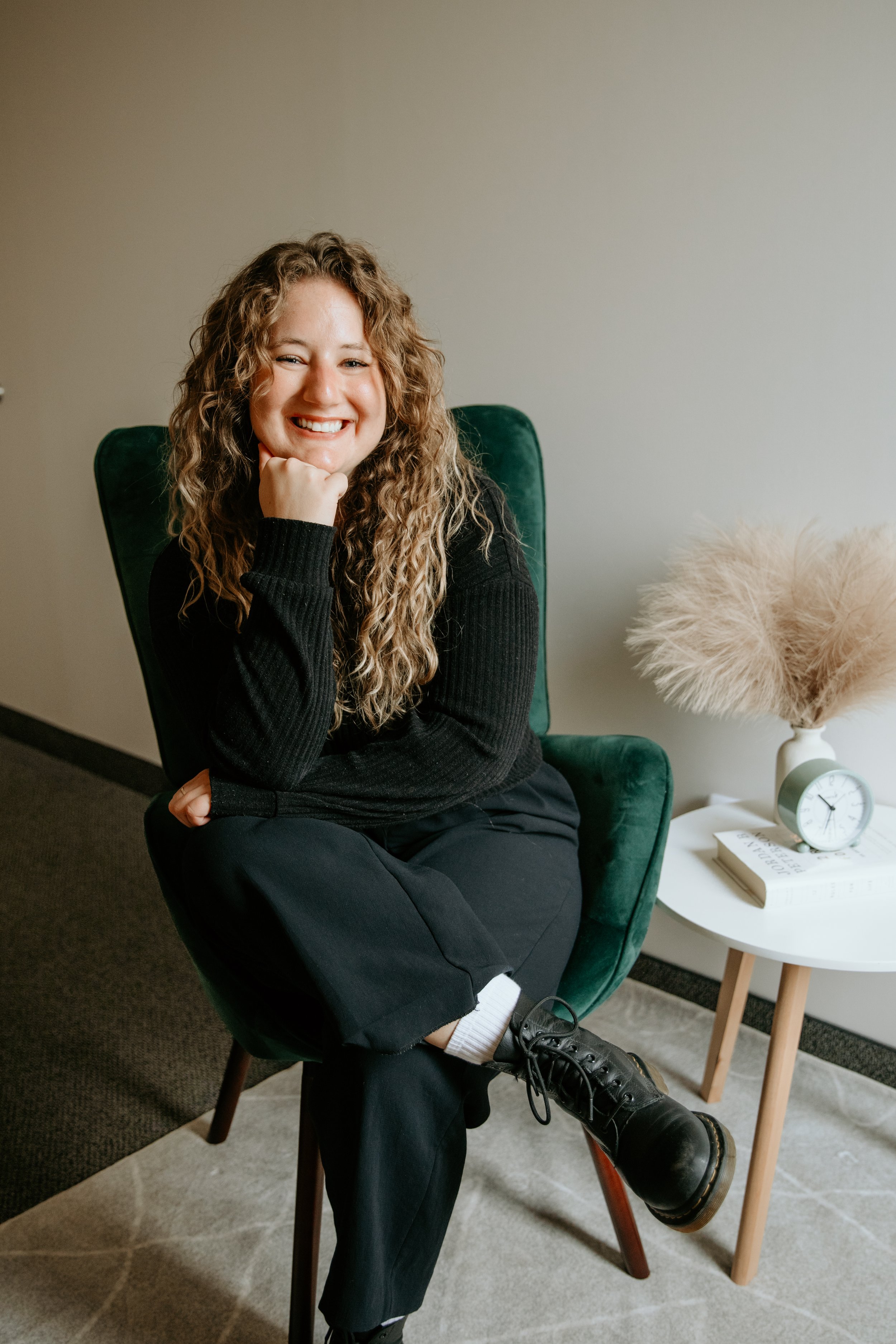 Person with curly hair and glasses wearing a knit sweater in front of an abstract painting.