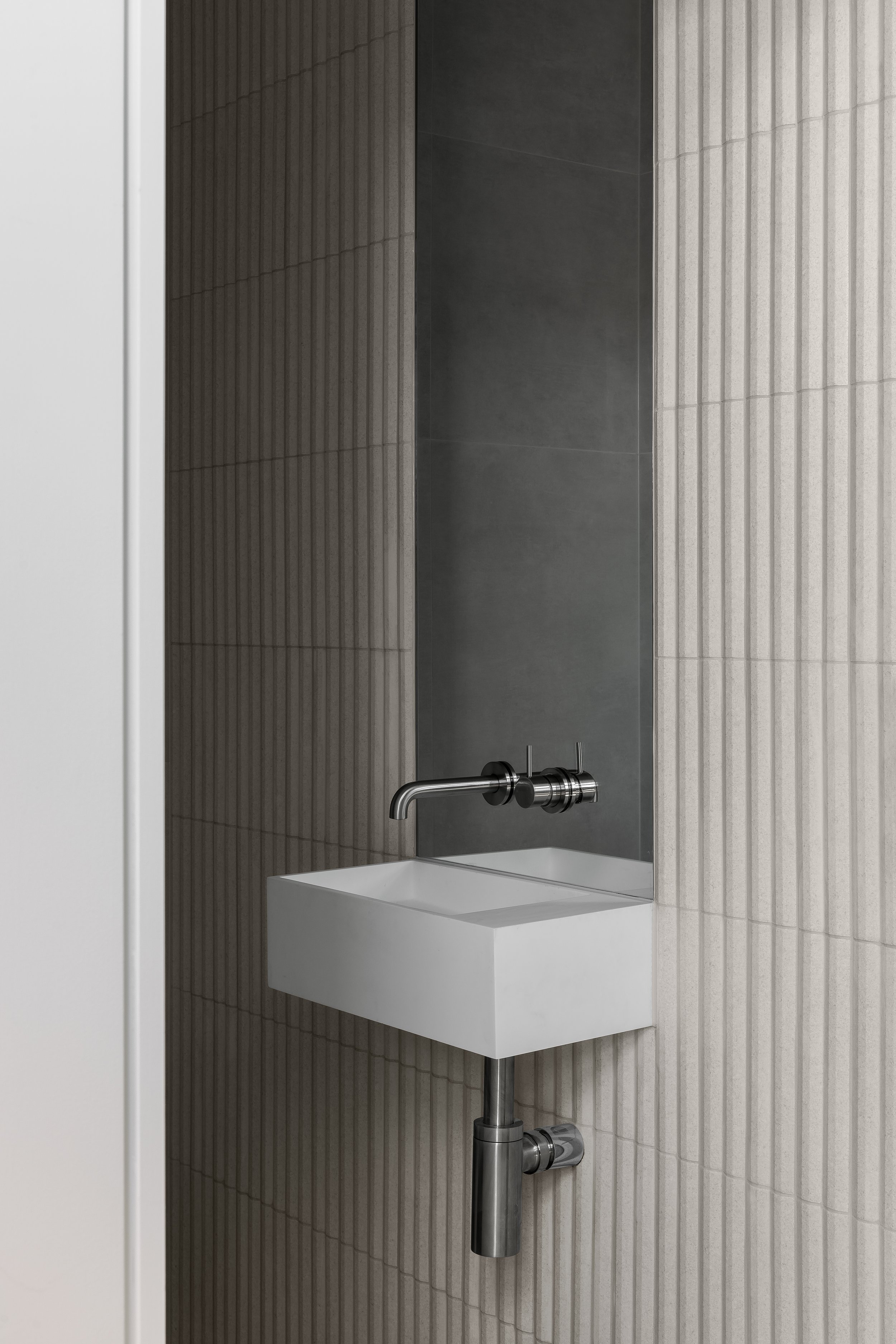 Minimalist bathroom sink with wall-mounted faucet and gray textured tiles.