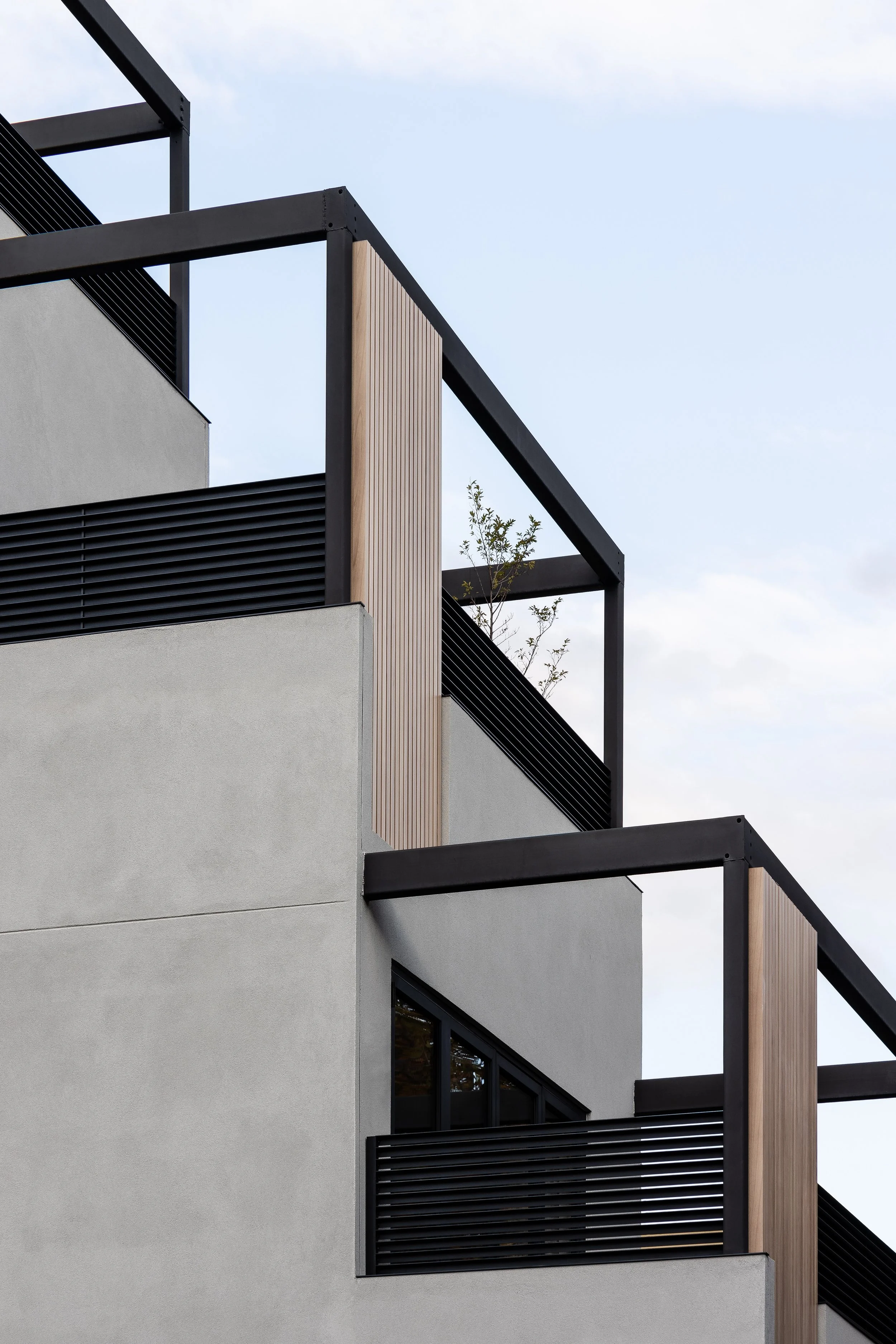 Modern architectural building with angular design and minimalistic features, including black metal railings and wooden panel accents.