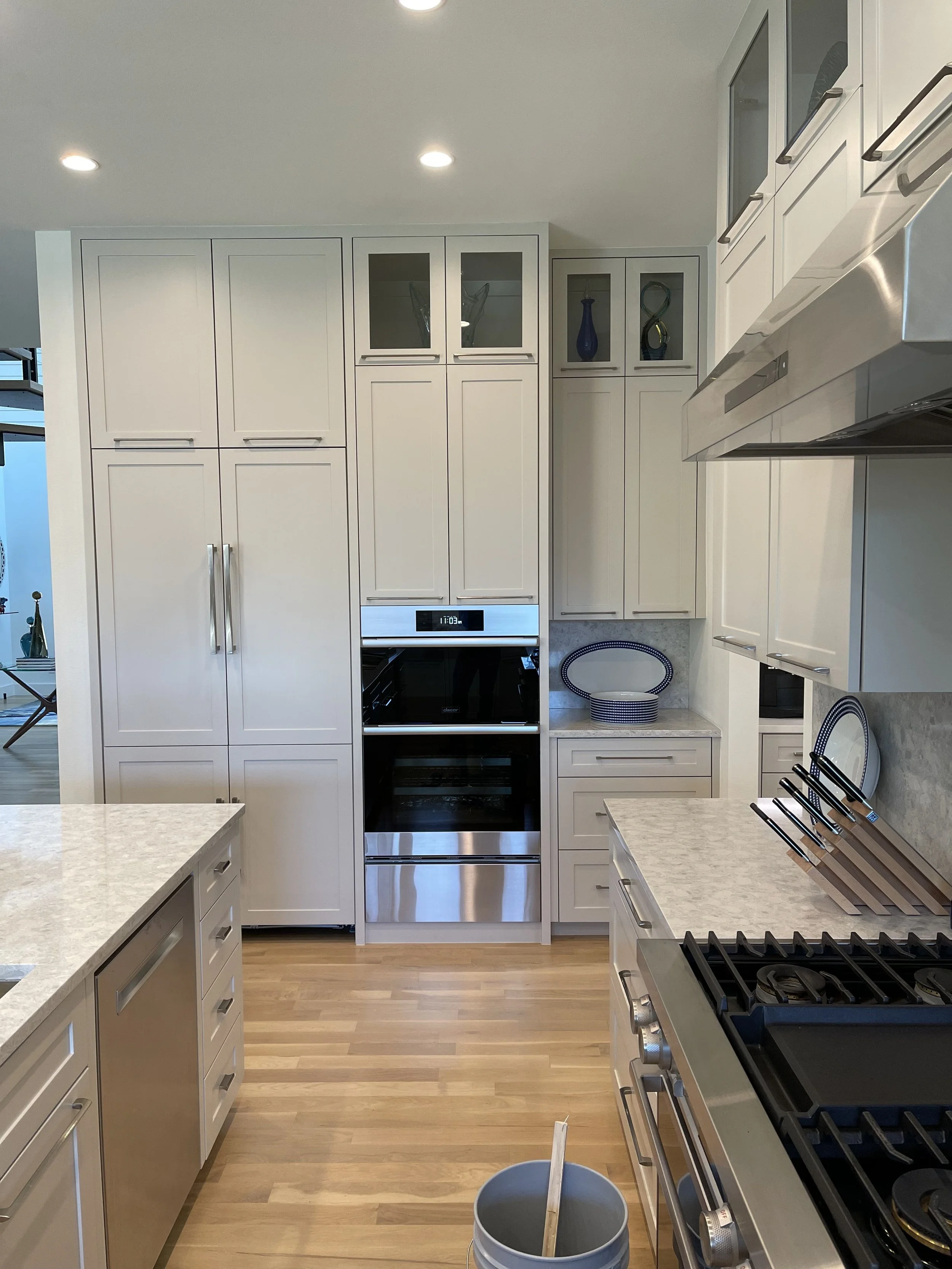 Modern bathroom with white walls, marble countertop, a white vessel sink, gold fixtures, hanging light bulbs, a large mirror, white cabinetry, a small window, and a decorative potted orchid plant.