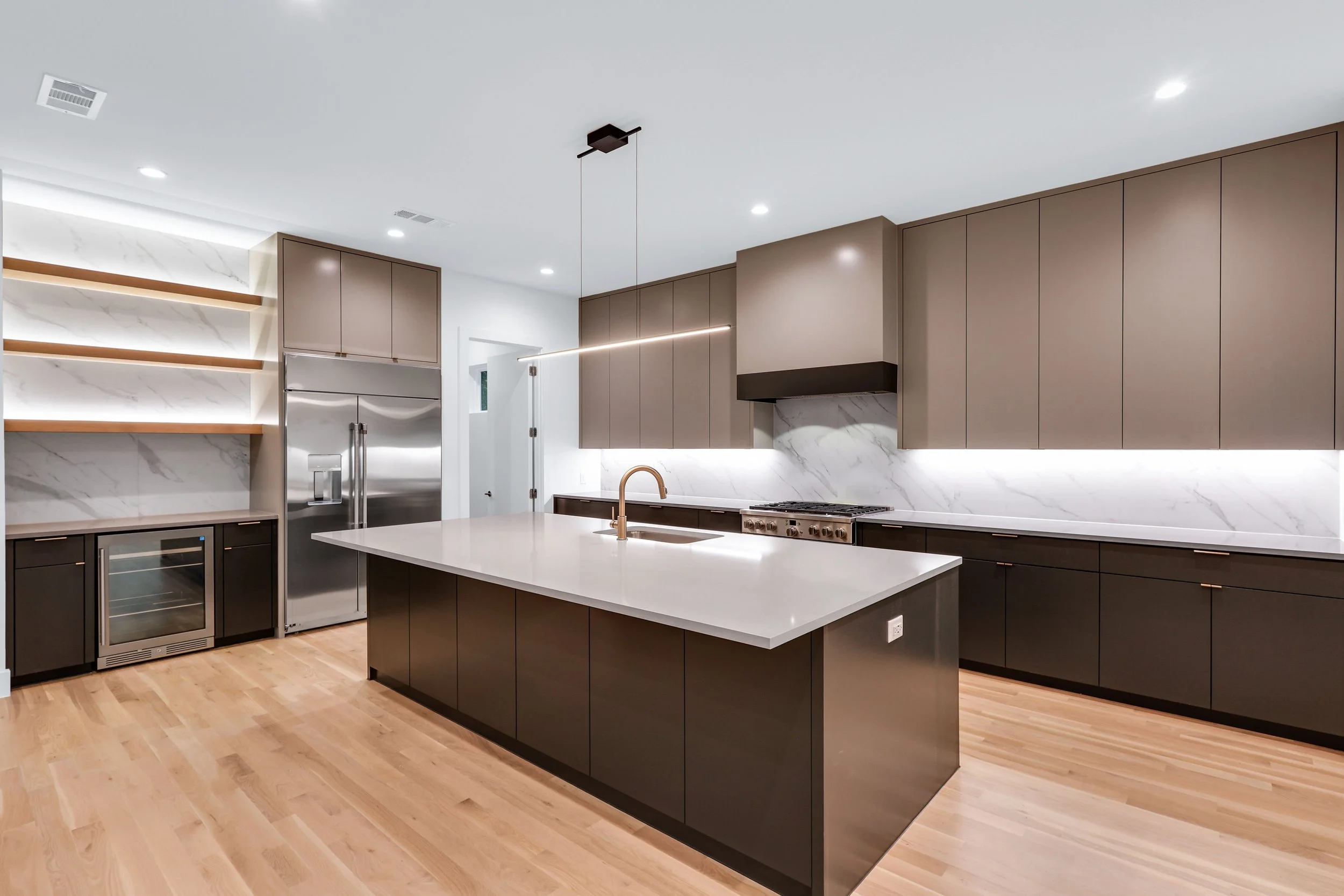 Modern kitchen with island, gray cabinets, marble backsplash, wooden shelves, and stainless steel appliances.