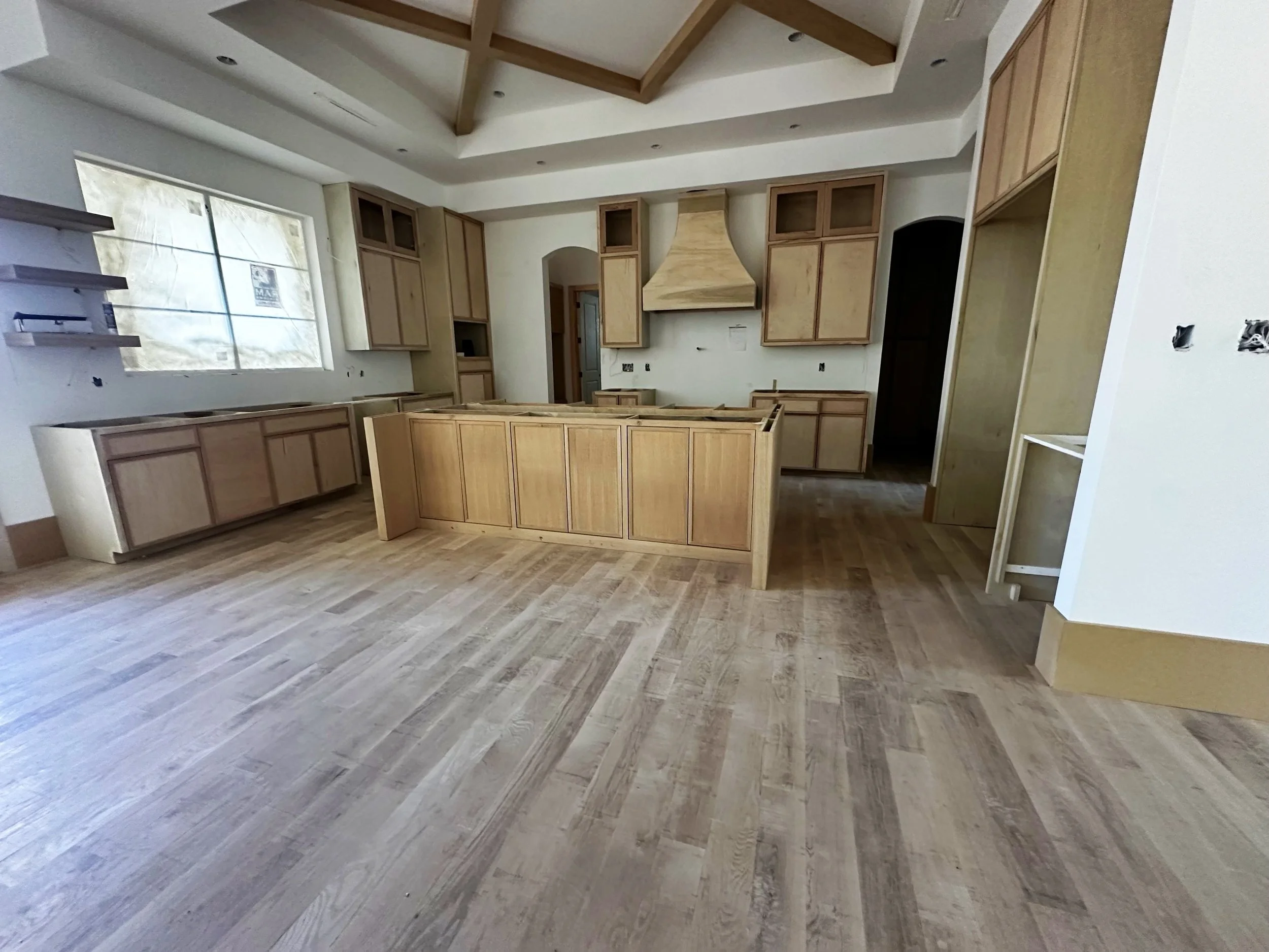 Unfinished kitchen with light wood cabinets, a central island, and a large window, during construction.