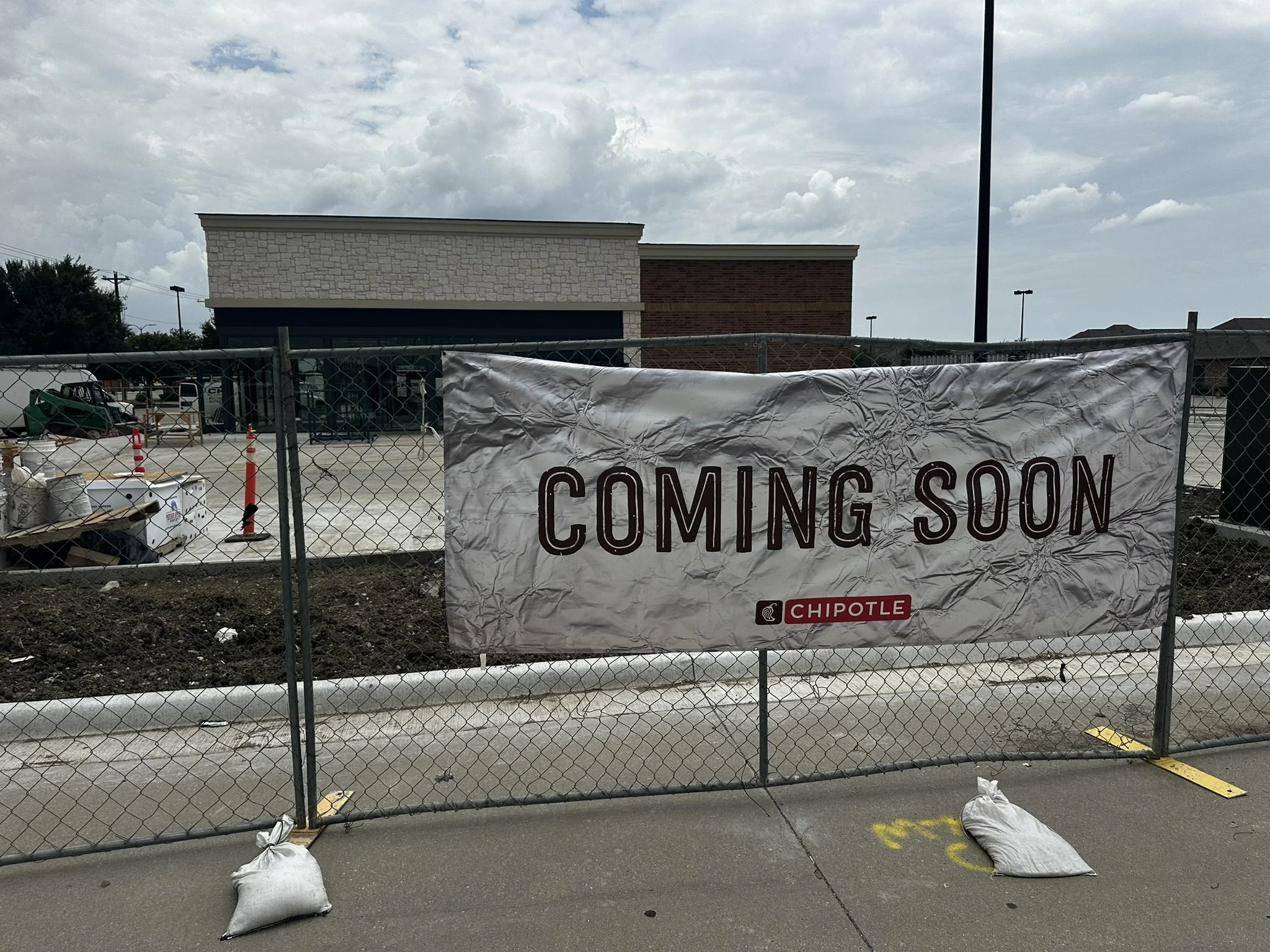 Construction fence with a sign that says "Coming Soon" and the Chipotle logo nearby, indicating a new restaurant opening.