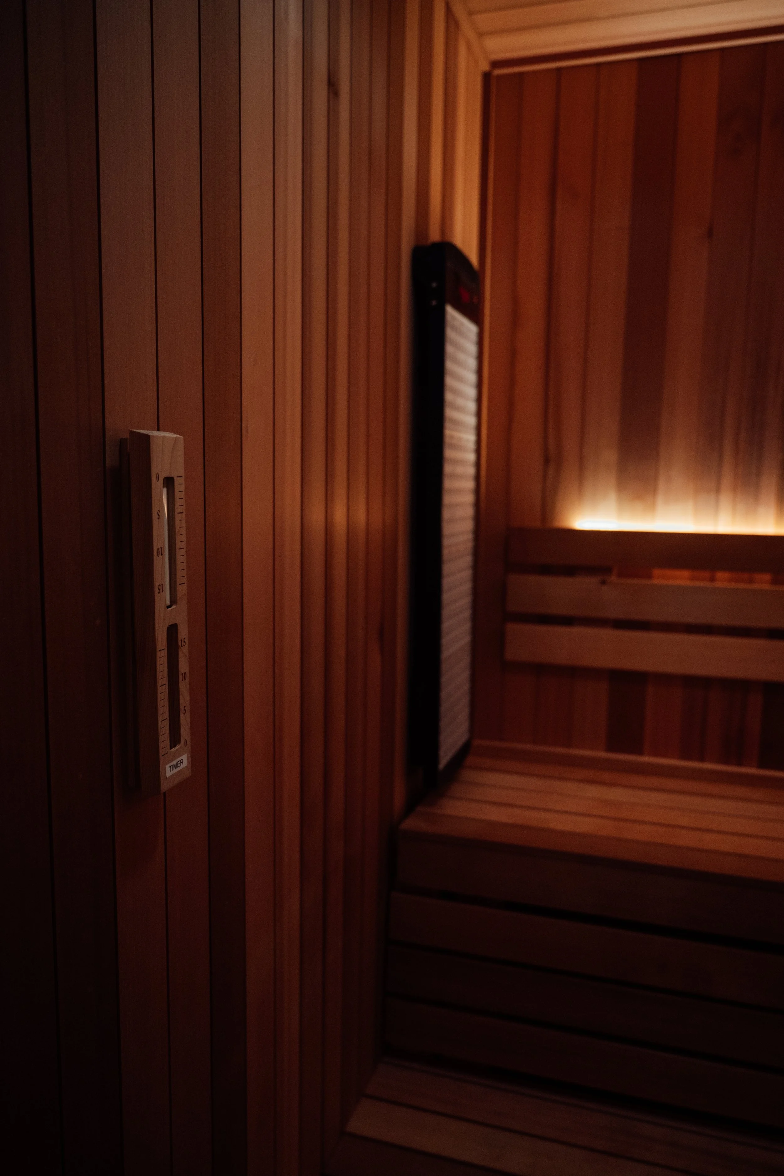 A wood-paneled sauna room with a thermometer on the wall and a bench.