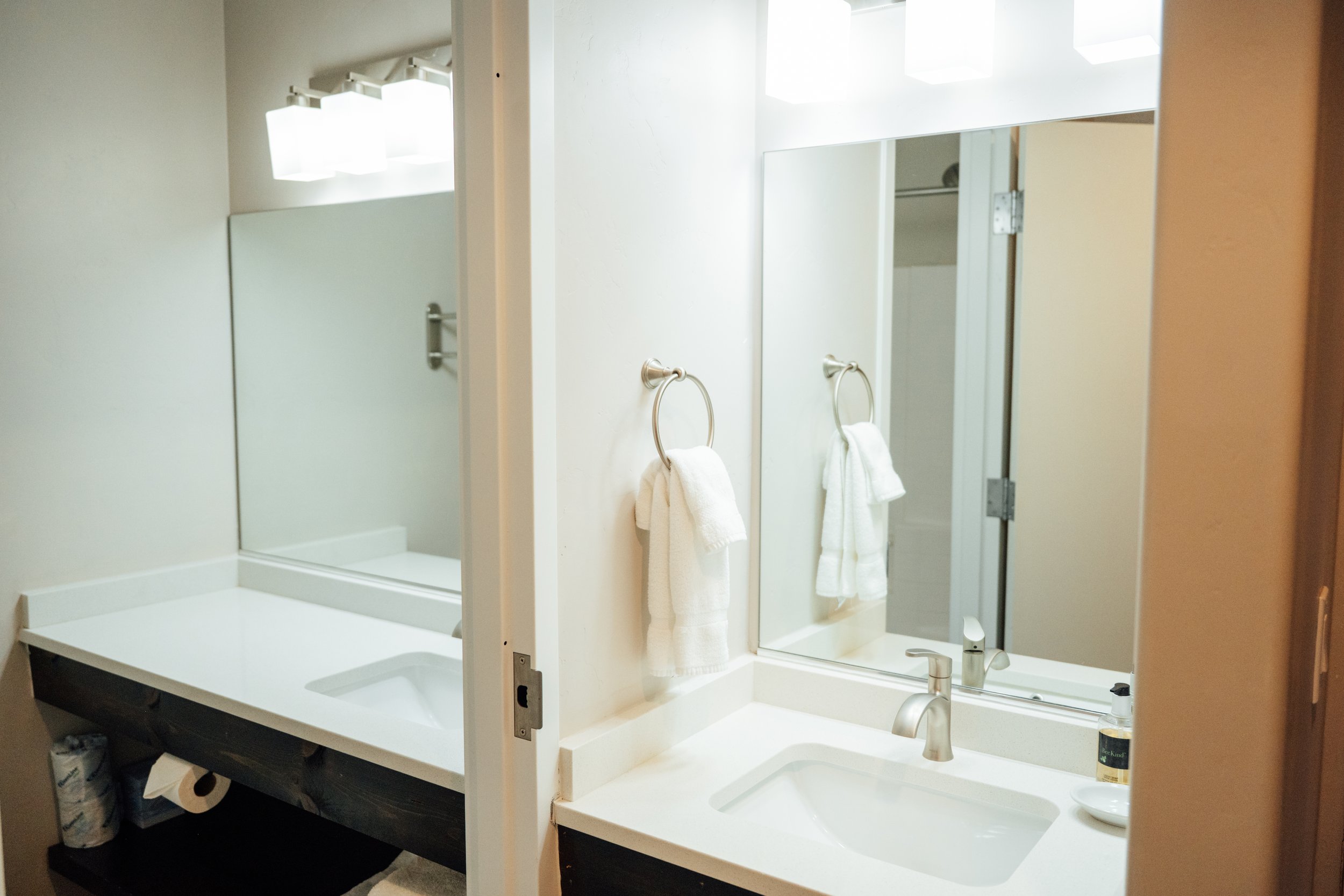 Movara double queen room bathroom vanity area with a large mirror, a sink with a faucet, towels hanging on towel rings, and a shower visible in the reflection.
