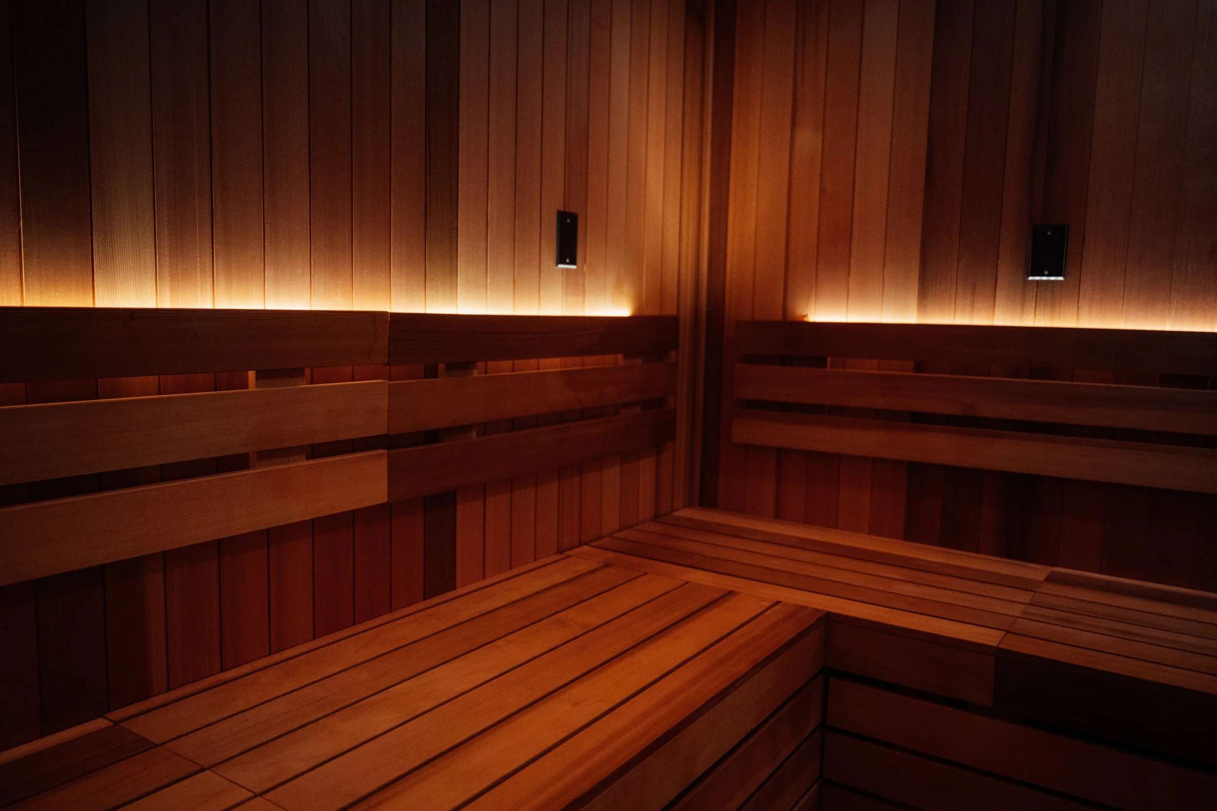 Wood-paneled sauna interior with built-in bench seating and subtle lighting.