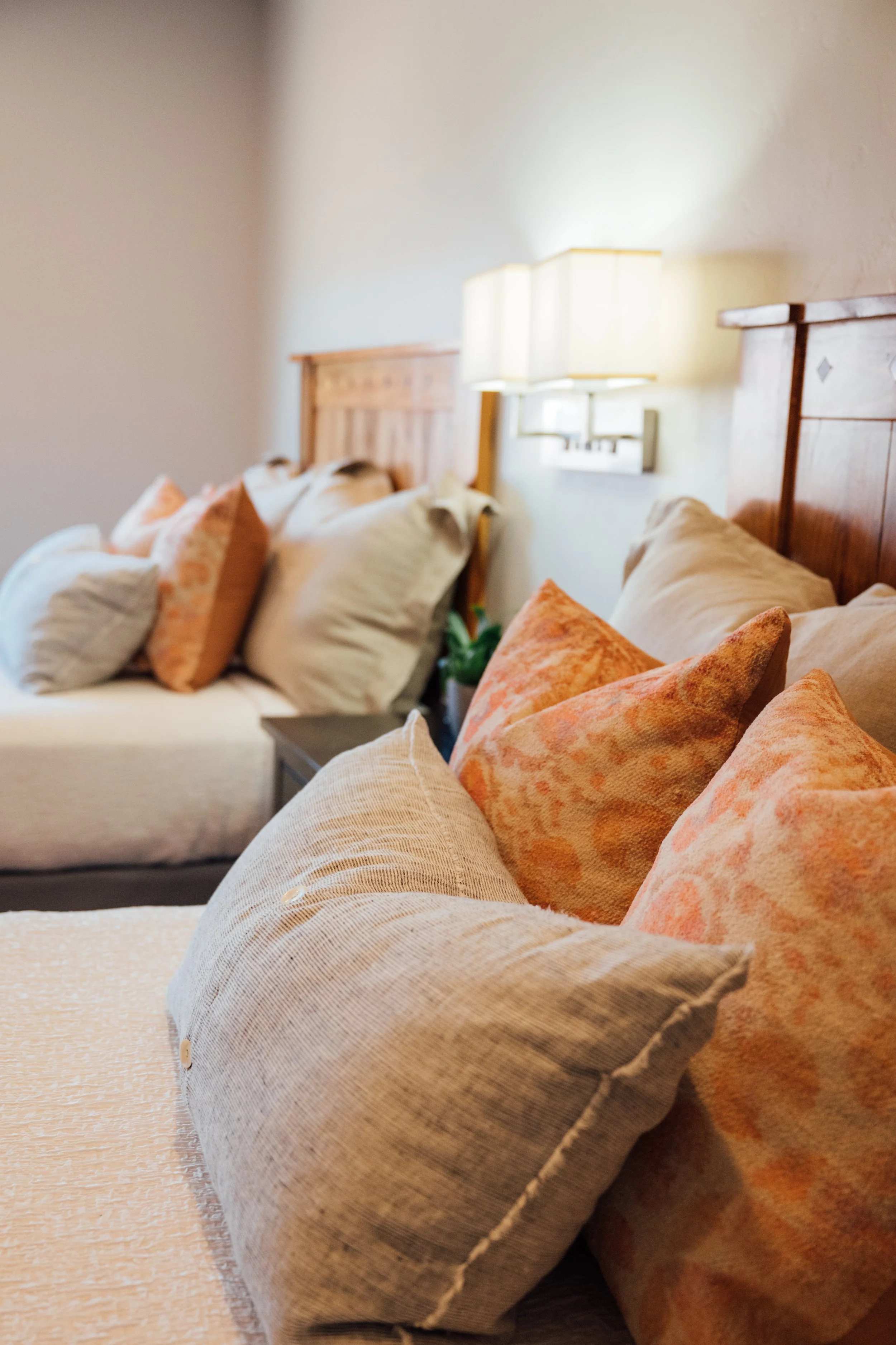 Close-up of a bed with tan and orange pillows in a cozy bedroom, with a wooden headboard and soft lighting.