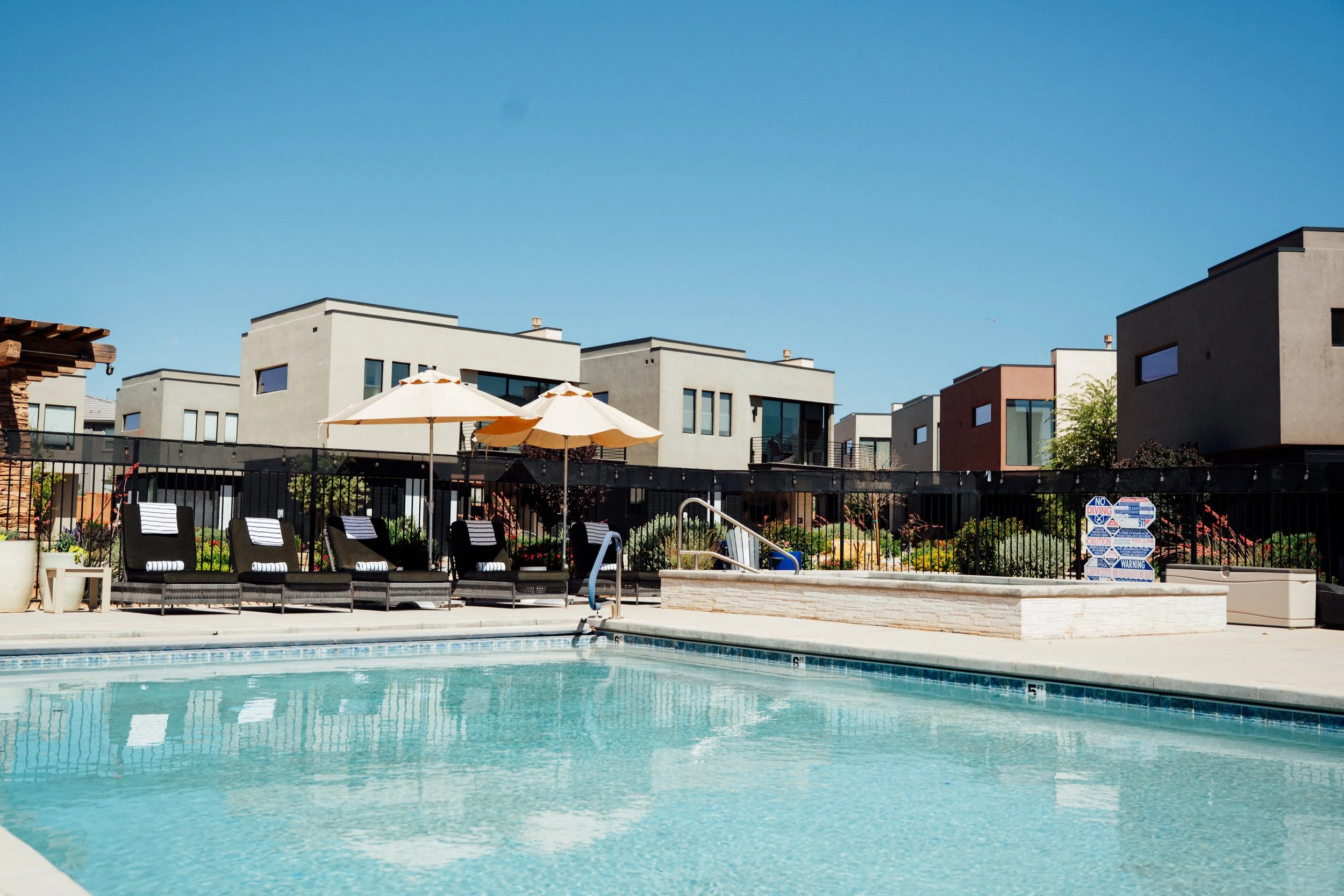 Movara Villa swimming pool with lounge chairs and umbrellas, surrounded by Villas under a clear blue sky.