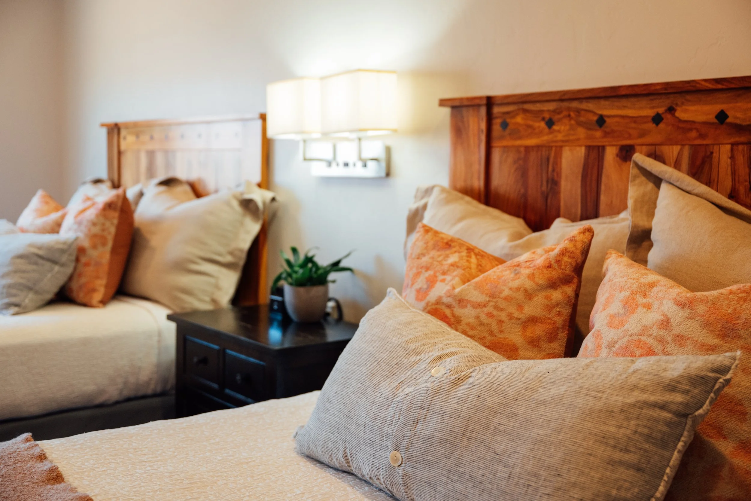 Hotel room with two beds, wooden headboards, white bedding, a wall-mounted TV, a desk with a chair, a window, and a ceiling fan.
