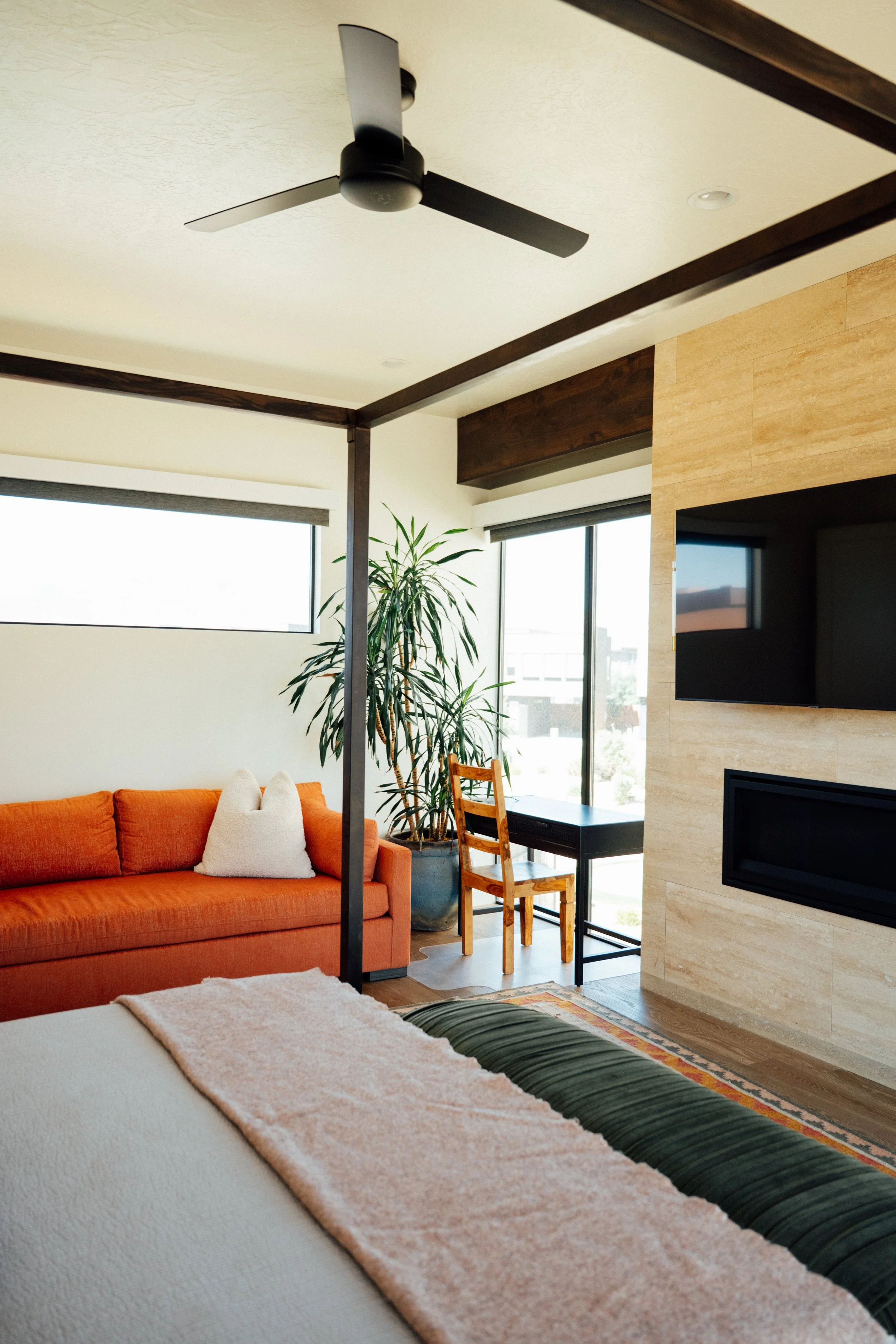 Movara Villa King Room with a living room with an orange sofa, white pillows, and a beige blanket on the white bed, near a large window with a green potted plant, a wooden chair, and a black table, with a wall-mounted TV and fireplace