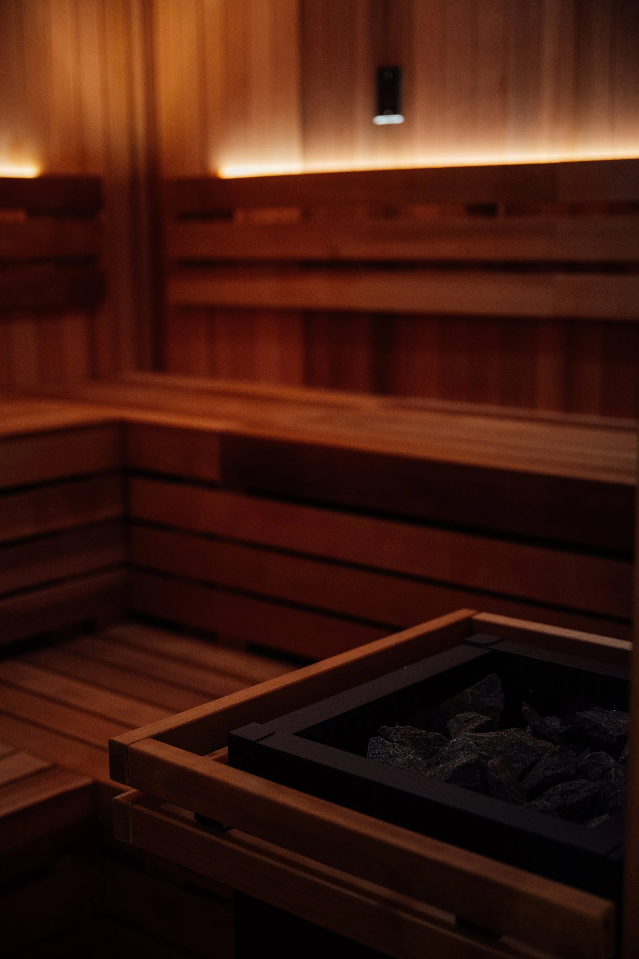 Inside a sauna room with wooden walls, benches, and a heated rock area for sauna stones.