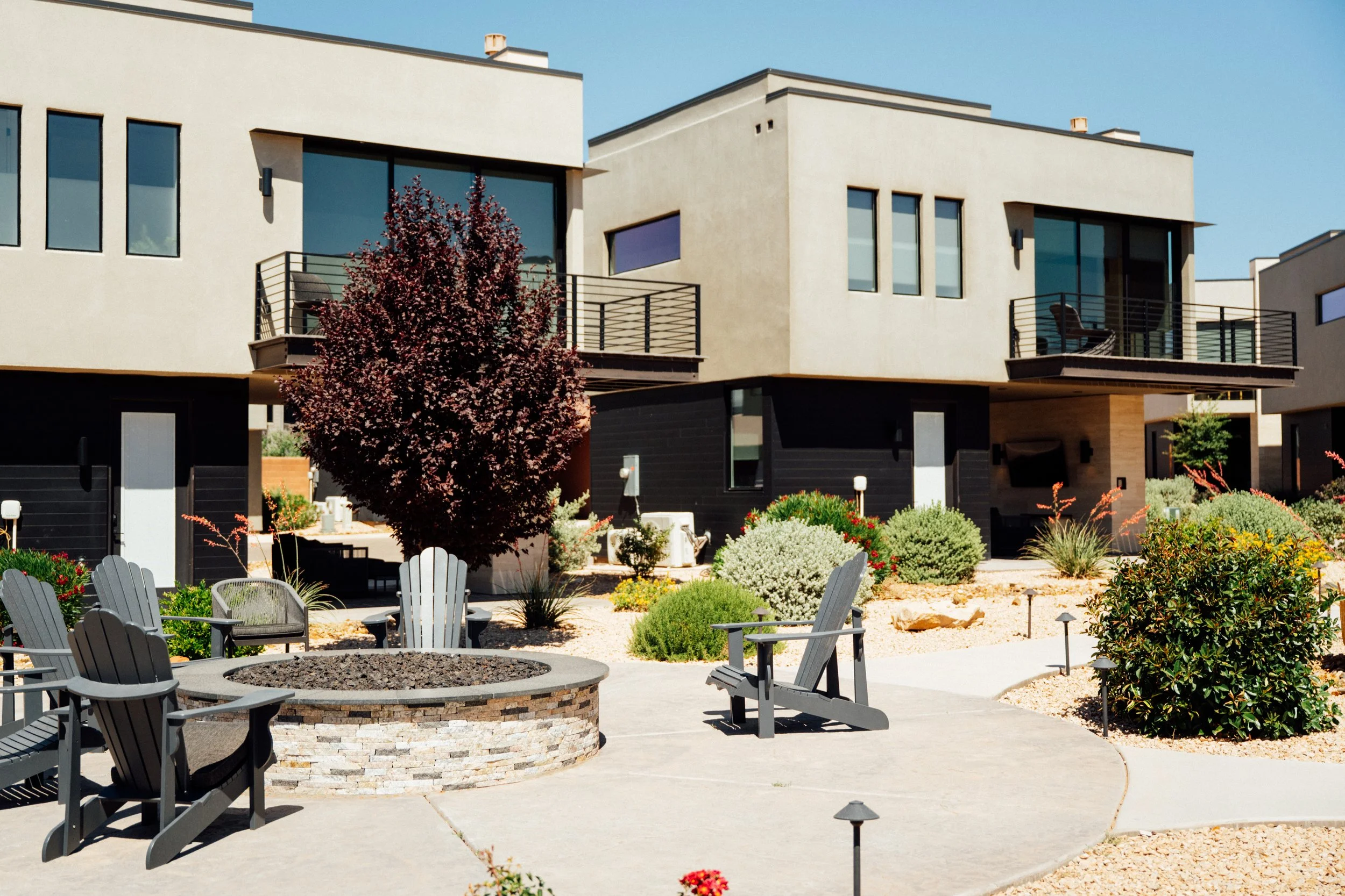 Modern residential buildings with outdoor seating area and landscaped garden featuring trees, bushes, and flowers.
