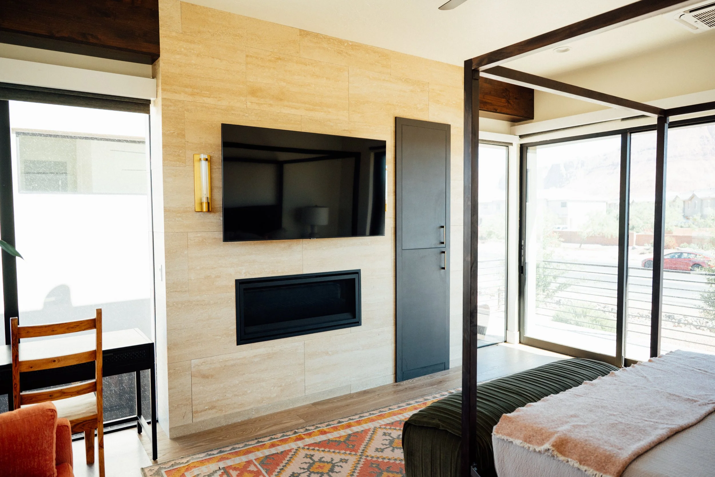 Movara Villa primary suite with Living room with a wall-mounted flat-screen TV, fireplace, large windows showing outside view, and a patterned rug.