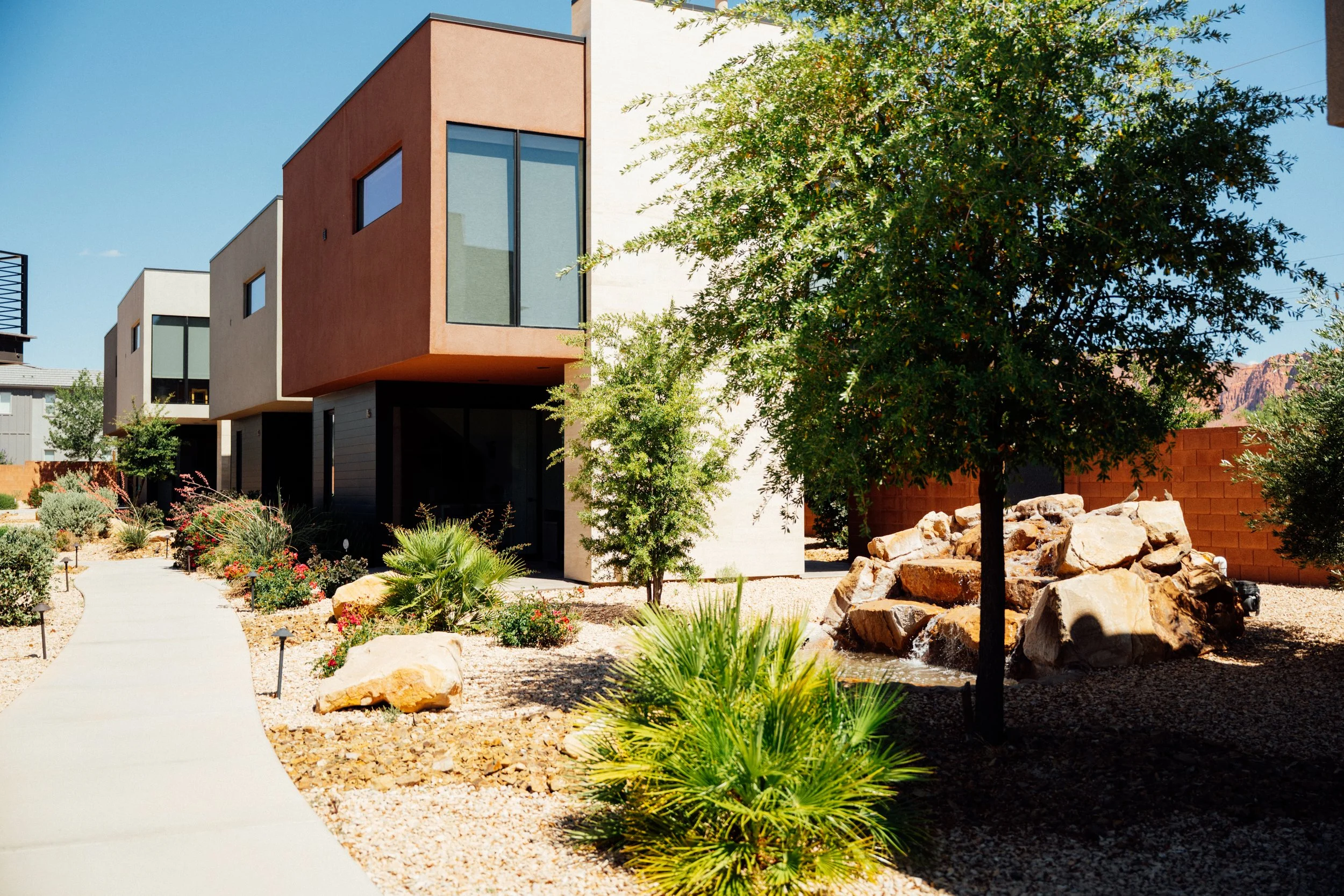 Movara Villas surrounded by desert landscaping including rocks, succulents, and small trees, with a clear blue sky in the background.