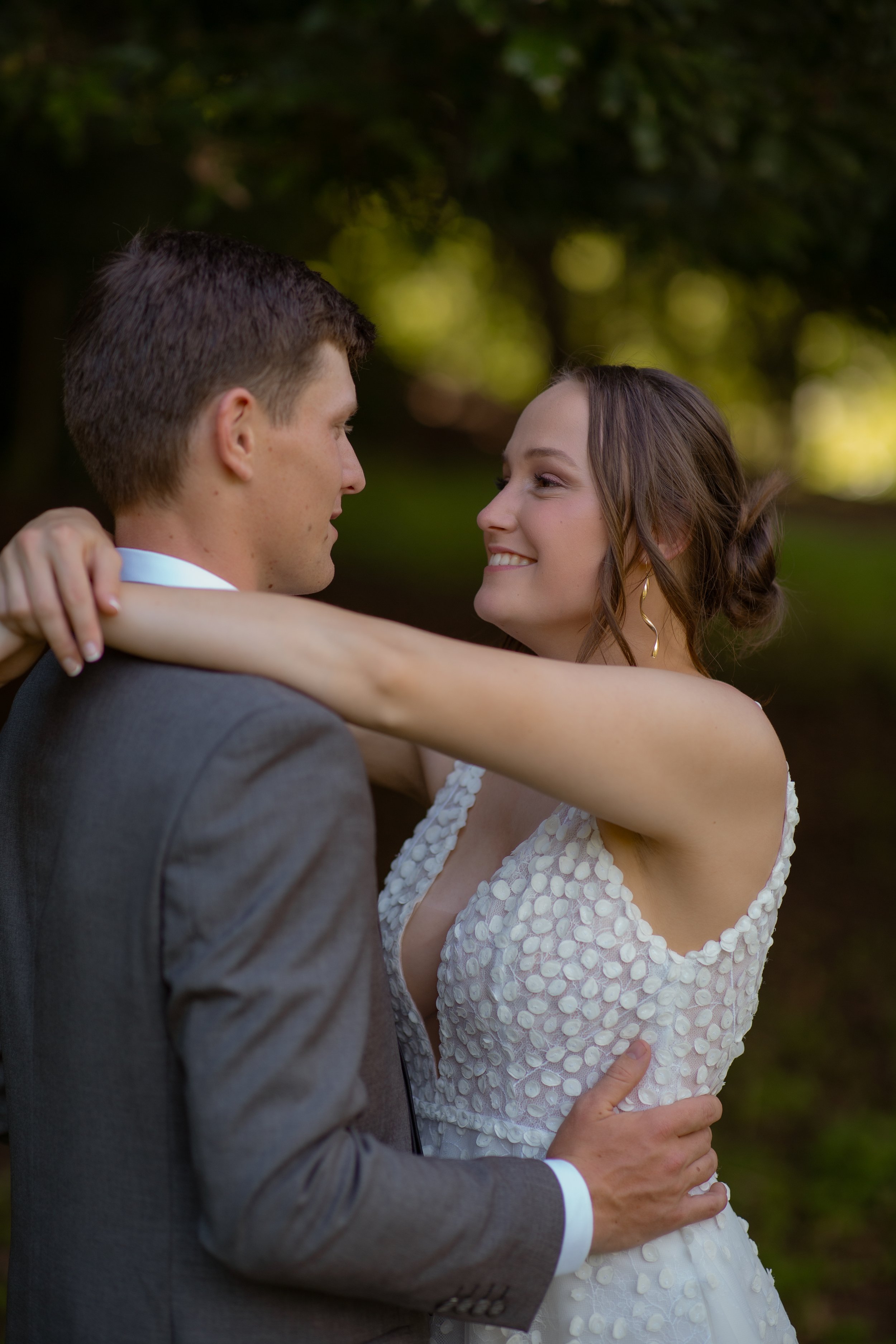 A bride and groom dance outdoors, looking into each other's eyes, with green trees in the background.  Wedding Photography Waikato New Zealand. Wedding Photography Hamilton New Zealand. Northland Wedding Photography