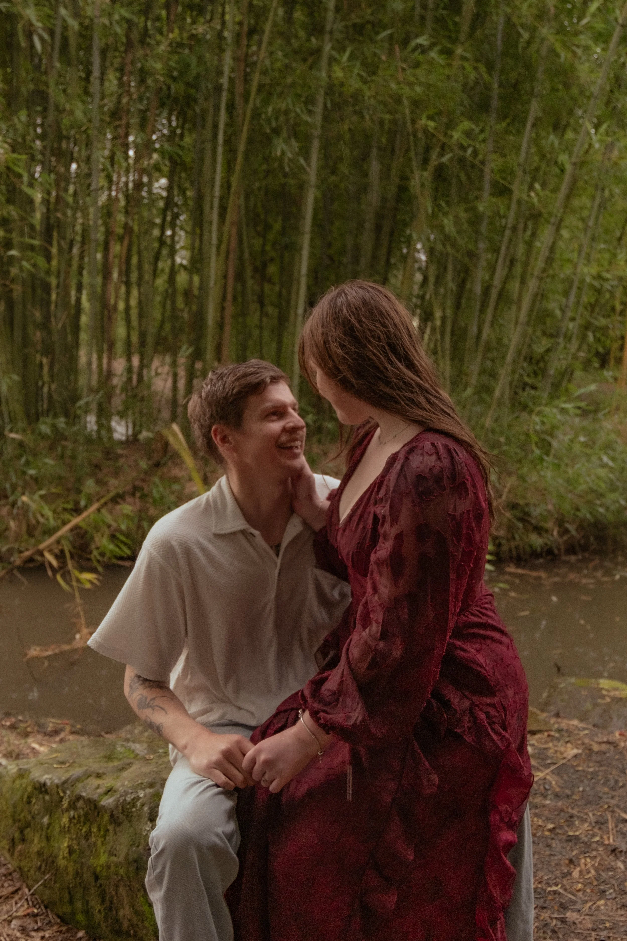 A man and woman sharing a joyful moment outdoors near a pond surrounded by bamboo. Couples photography Hamilton New Zealand. Engagement photography Hamilton New Zealand. Whangarei New Zealand Couples photographer