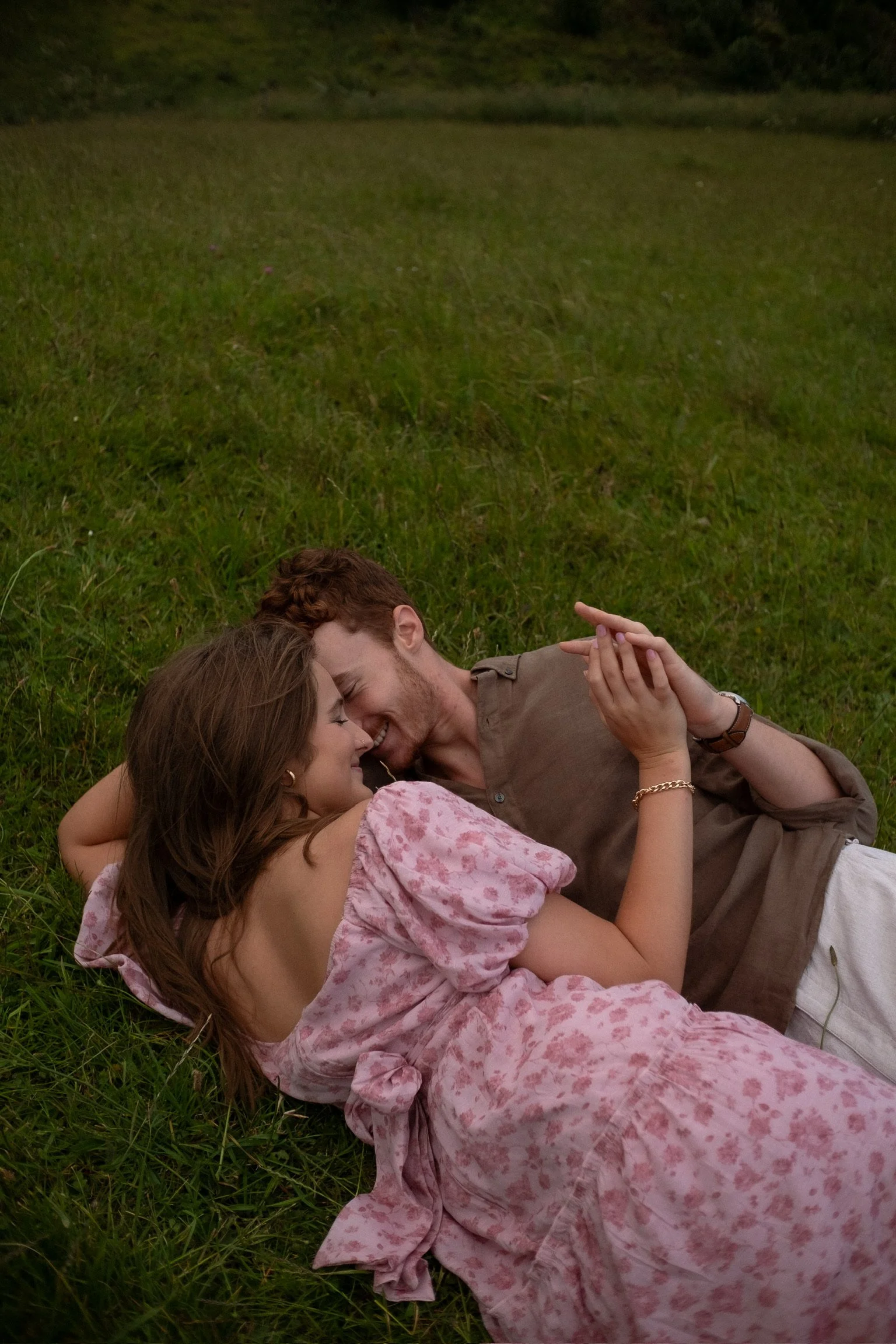 A couple laying on the grass, smiling and cuddling each other. Couples photography Raglan New Zealand. Engagement photography Hamilton New Zealand. Whangarei New Zealand Couples photographer