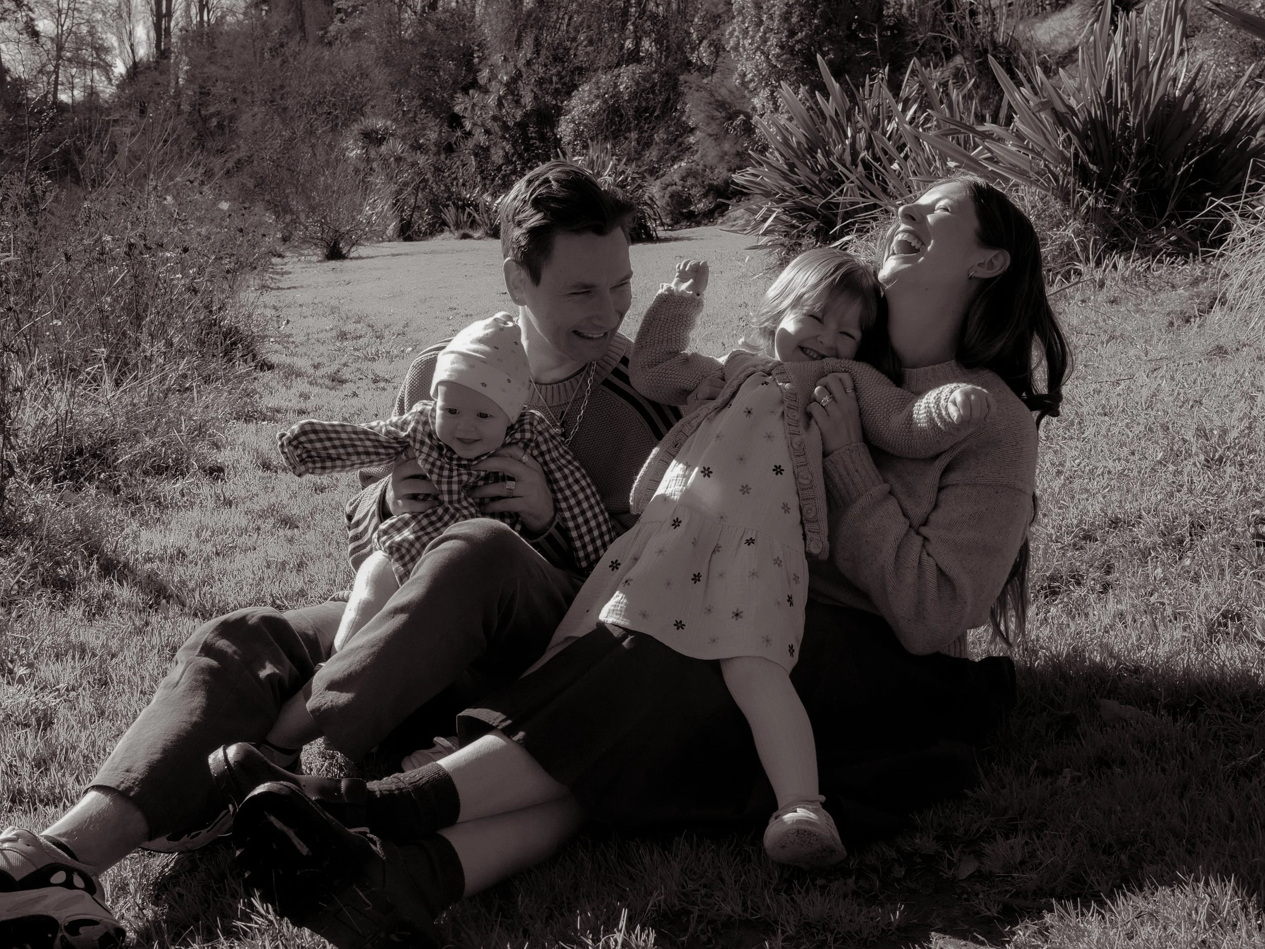 A family of four sitting on grass outdoors, laughing and playing together. Family Photography Waikato New Zealand. Family Photography Hamilton New Zealand. Northland Wedding Photography