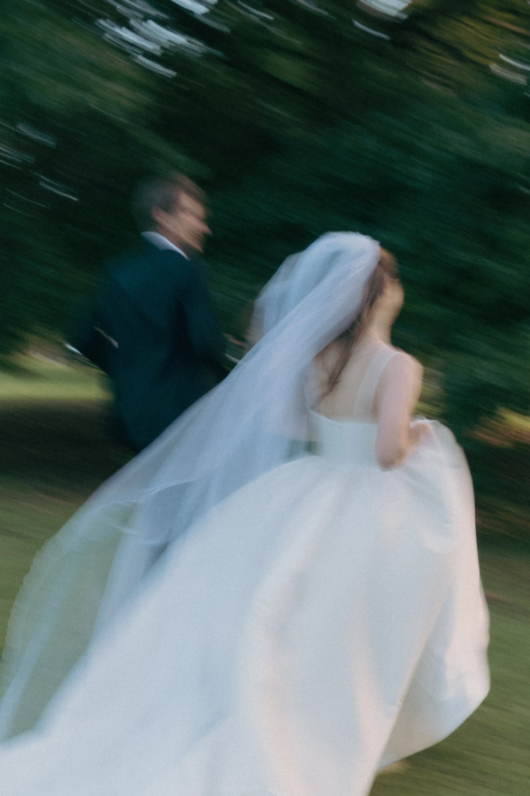 A blurry photo of a bride and groom walking outdoors with a background of green trees, possibly at a wedding or formal event.