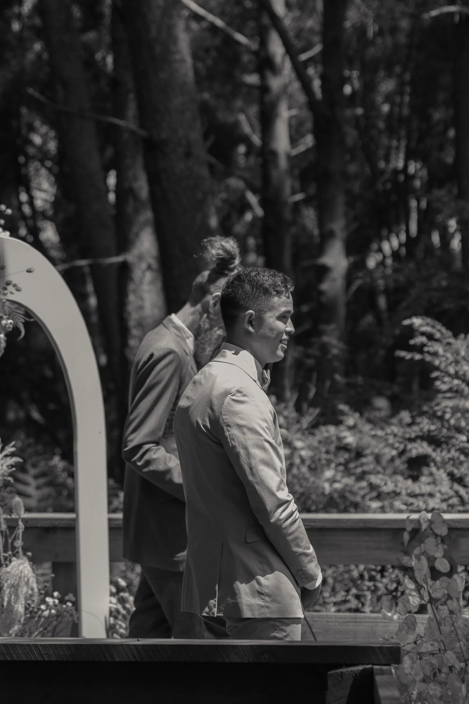 Two men in suits standing outdoors on a wooden platform with trees in the background.  Wedding Photography Waikato New Zealand. Wedding Photography Hamilton New Zealand. Northland Wedding Photography