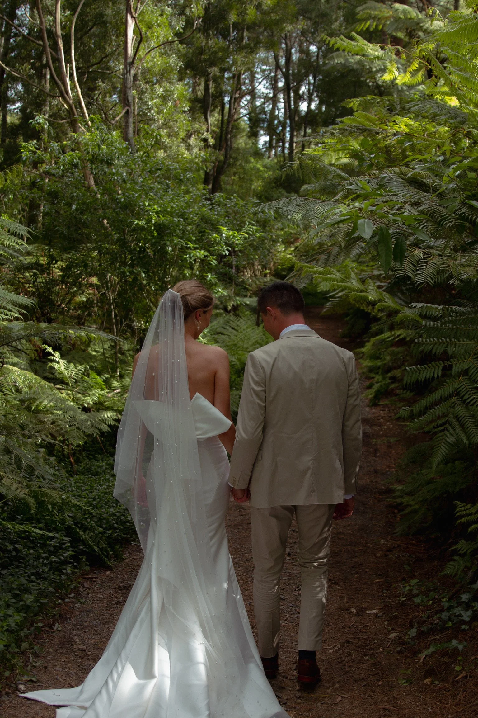 A bride and groom walking hand in hand through a wooded trail during their wedding.  Wedding Photography Waikato New Zealand. Wedding Photography Hamilton New Zealand. Northland Wedding Photography