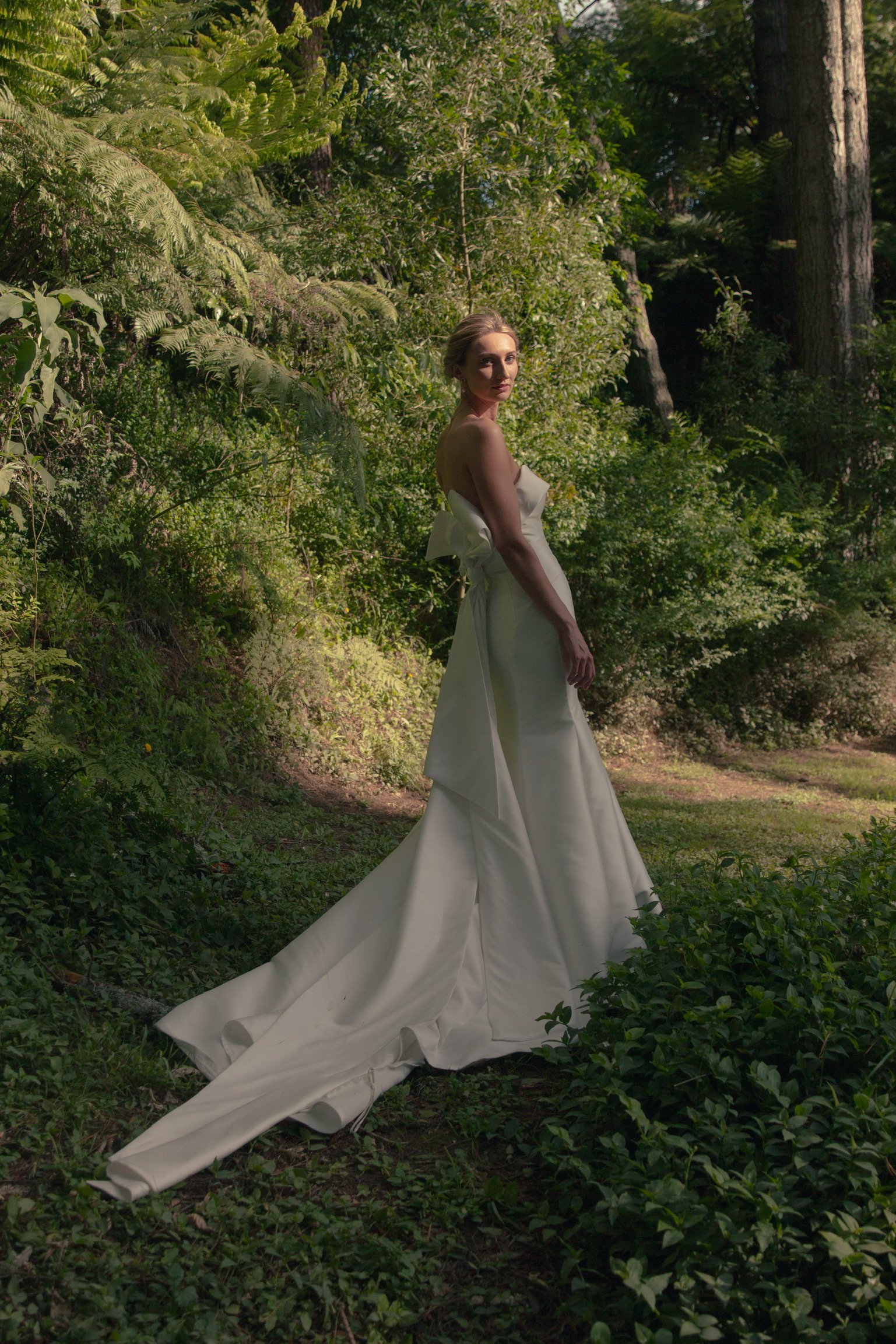 A woman in a white gown standing in a lush green forest.  Wedding Photography Waikato New Zealand. Wedding Photography Hamilton New Zealand. Northland Wedding Photography