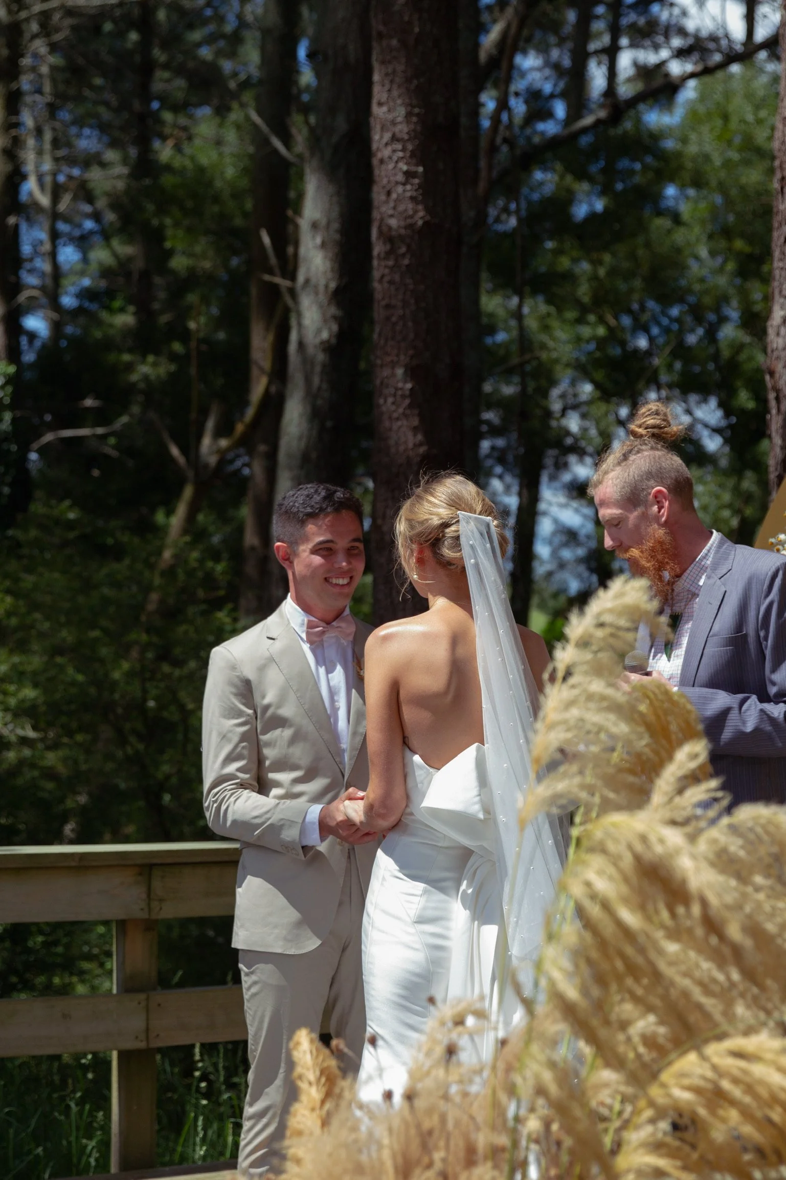 A couple getting married outdoors in a forest, with a man officiating, during daytime.  Wedding Photography Waikato New Zealand. Wedding Photography Hamilton New Zealand. Northland Wedding Photography