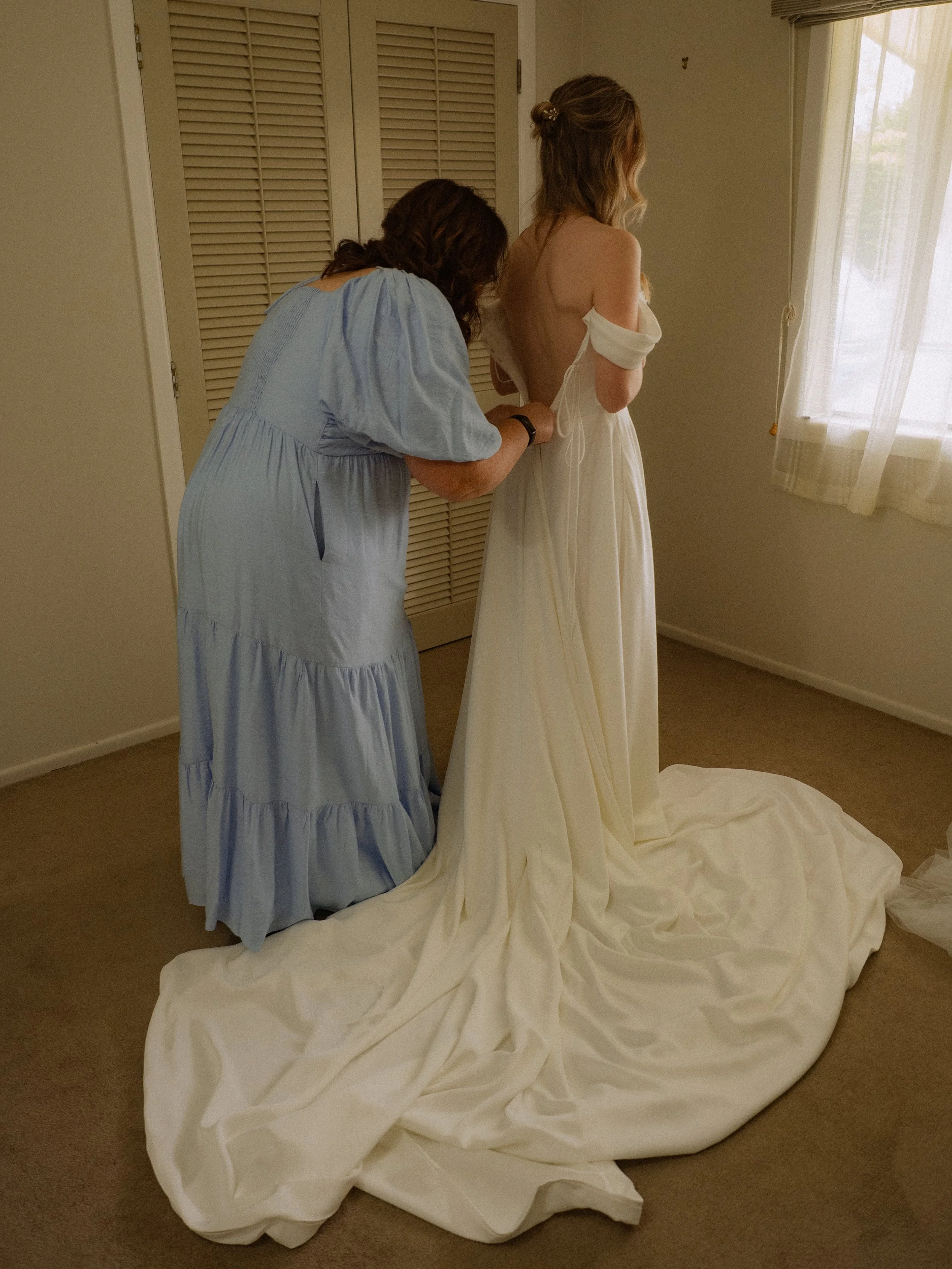 A woman helping another woman into a wedding dress in a bedroom.  Wedding Photography Waikato New Zealand. Wedding Photography Hamilton New Zealand. Northland Wedding Photography