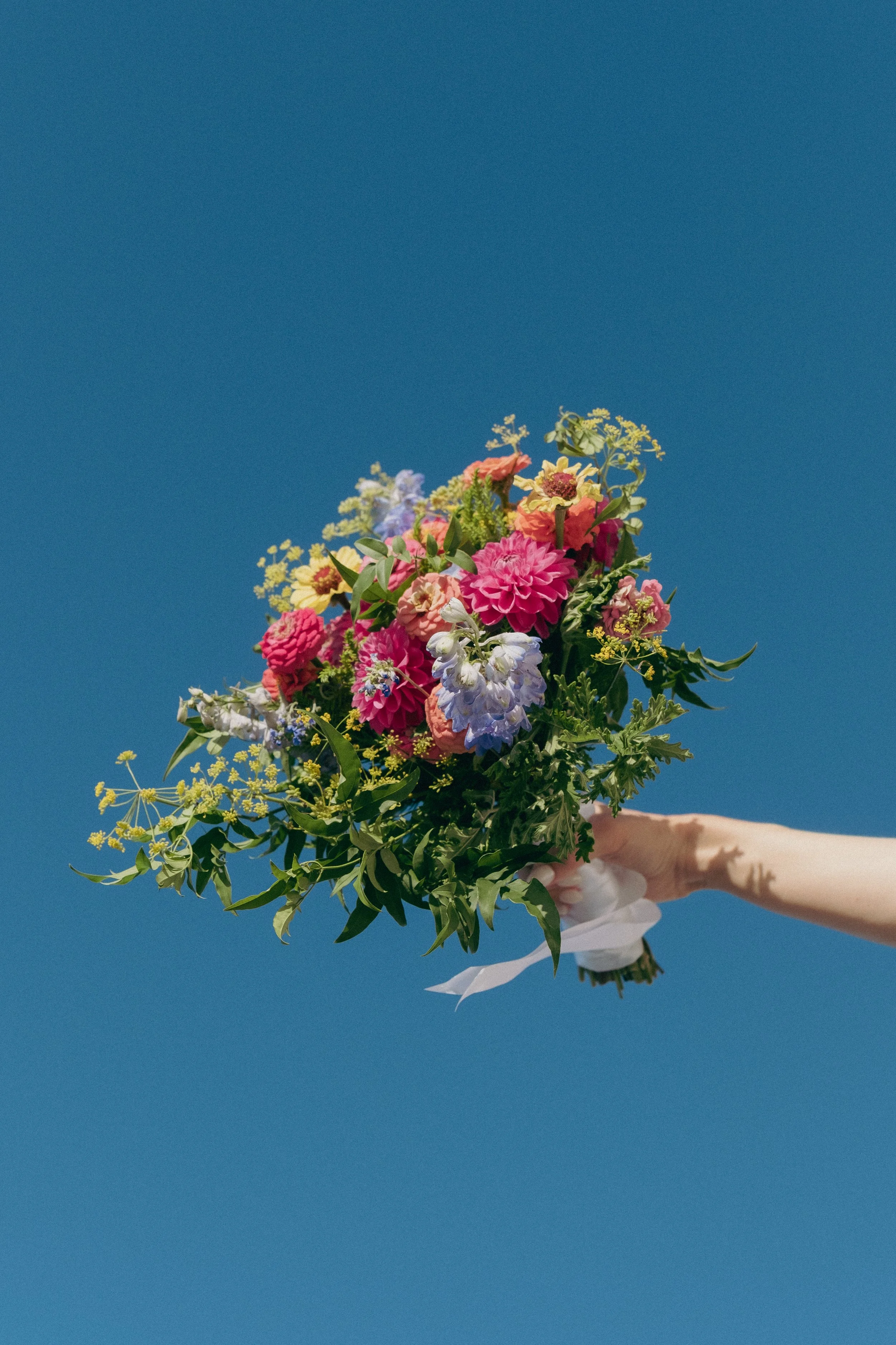 A person holding a colorful bouquet of flowers against a clear blue sky.