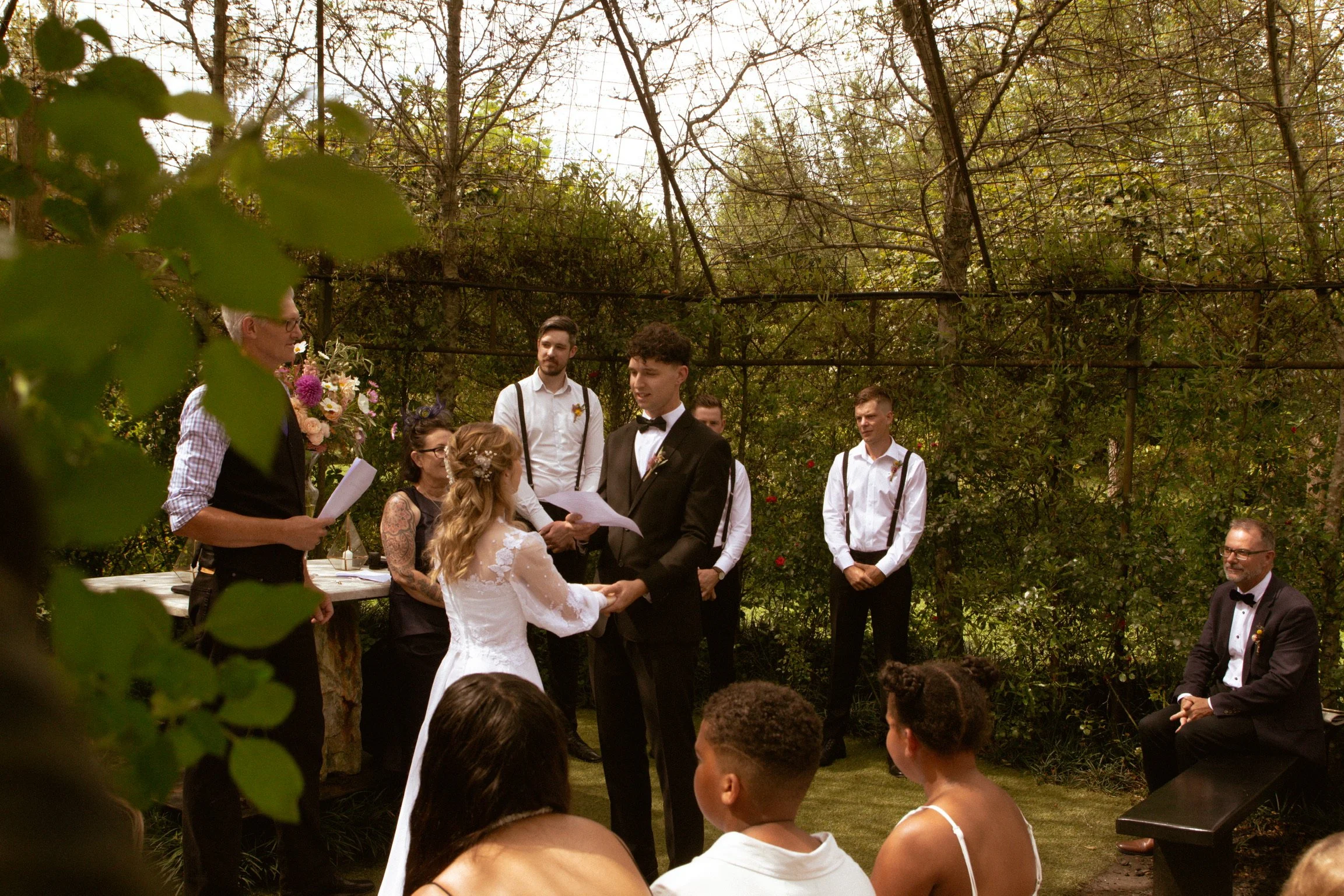 A couple gets married outdoors with officiant and witnesses present, surrounded by greenery and trees. Wedding Photography Waikato New Zealand. Wedding Photography Hamilton New Zealand