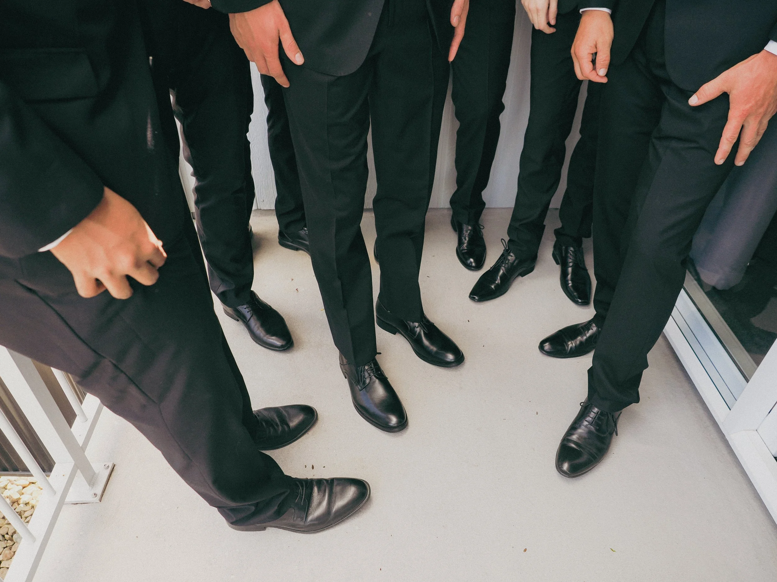 Group of people standing closely together, all dressed in black suits and black shoes, with only their lower bodies visible.