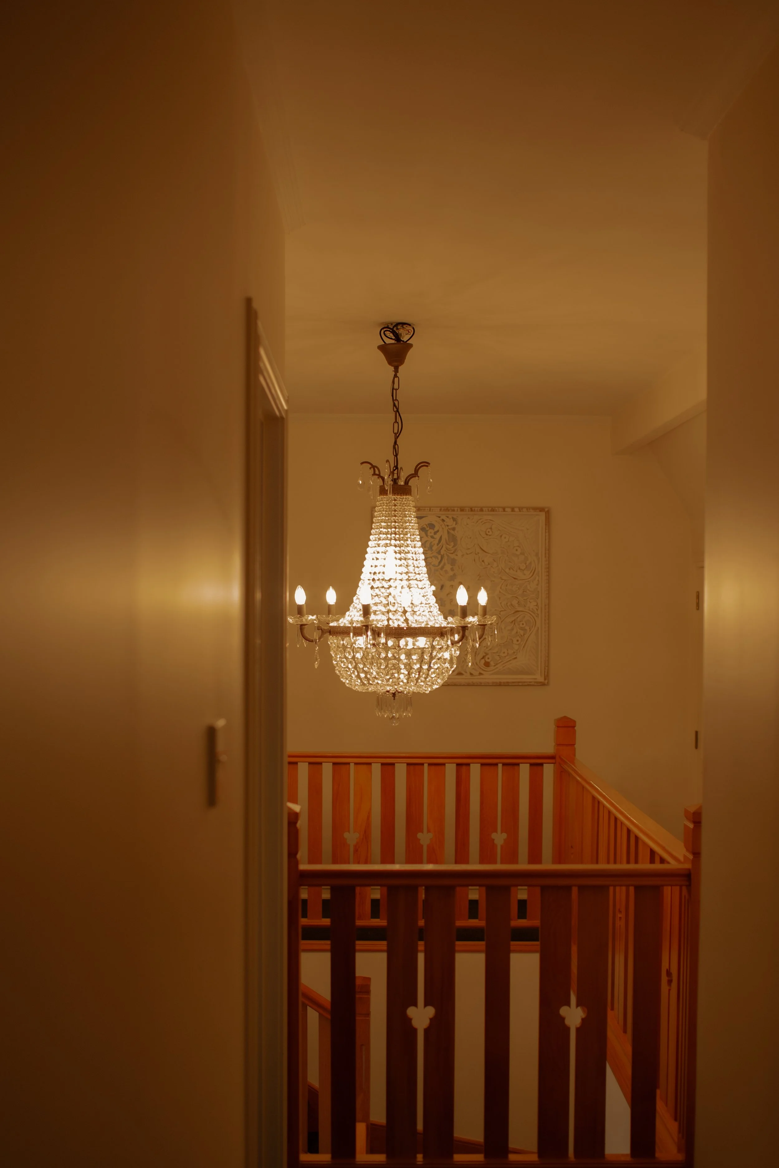 A chandelier hanging from the ceiling in a house, illuminating a stairwell with wooden railings.  Wedding Photography Waikato New Zealand. Wedding Photography Hamilton New Zealand. Northland Wedding Photography