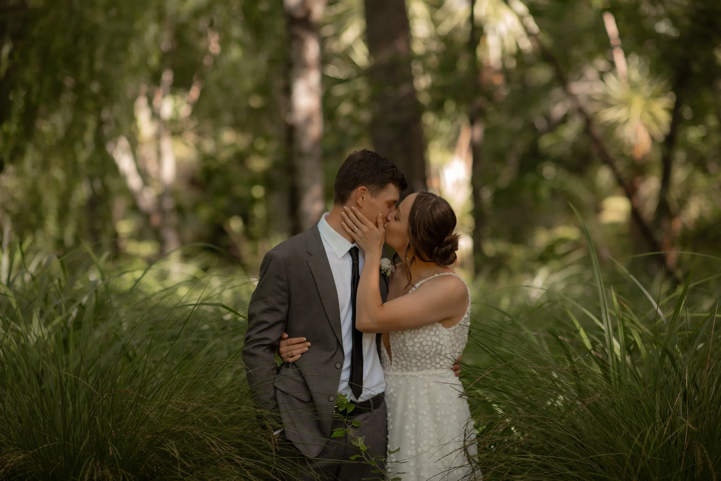 A bride and groom share a kiss and embrace in a lush, green forest.  Wedding Photography Waikato New Zealand. Wedding Photography Hamilton New Zealand. Northland Wedding Photography