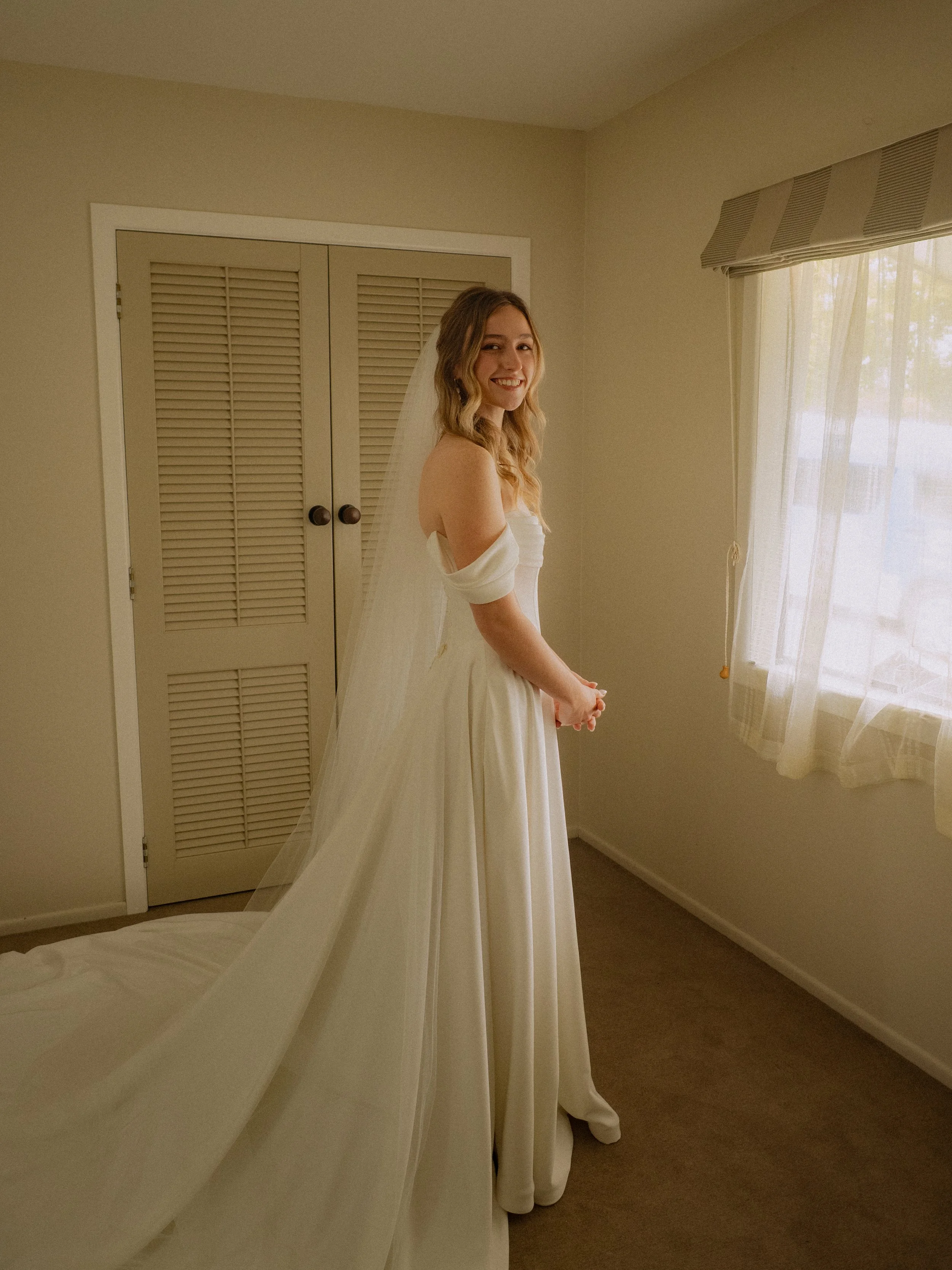 A young woman in a white wedding gown and veil standing in a bedroom, smiling at the camera.  Wedding Photography Waikato New Zealand. Wedding Photography Hamilton New Zealand. Northland Wedding Photography