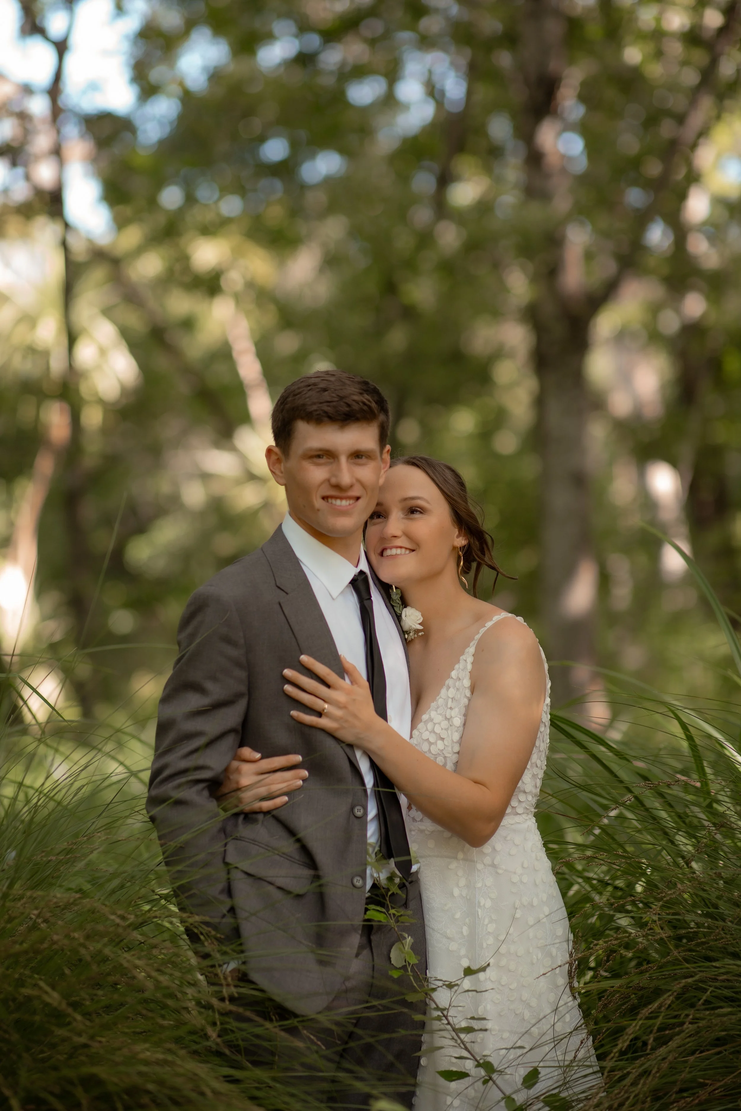 A happy bride and groom embracing outdoors in a wooded area, smiling at the camera.  Wedding Photography Waikato New Zealand. Wedding Photography Hamilton New Zealand. Northland Wedding Photography