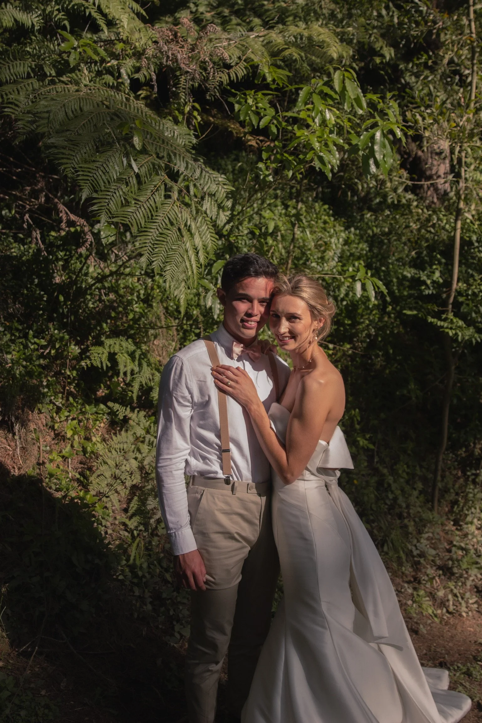 A bride and groom in wedding attire hugging in a lush green outdoor setting.  Wedding Photography Waikato New Zealand. Wedding Photography Hamilton New Zealand. Northland Wedding Photography