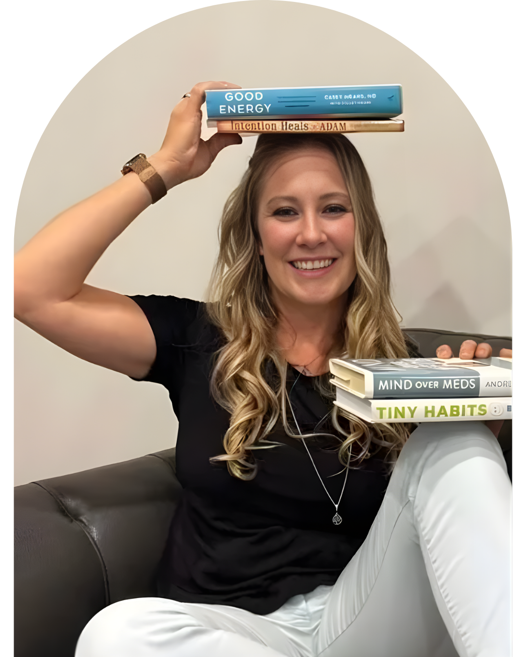 A young woman with blonde hair tied back, wearing a black top, a necklace, and a nose ring, smiling at the camera against a plain background.