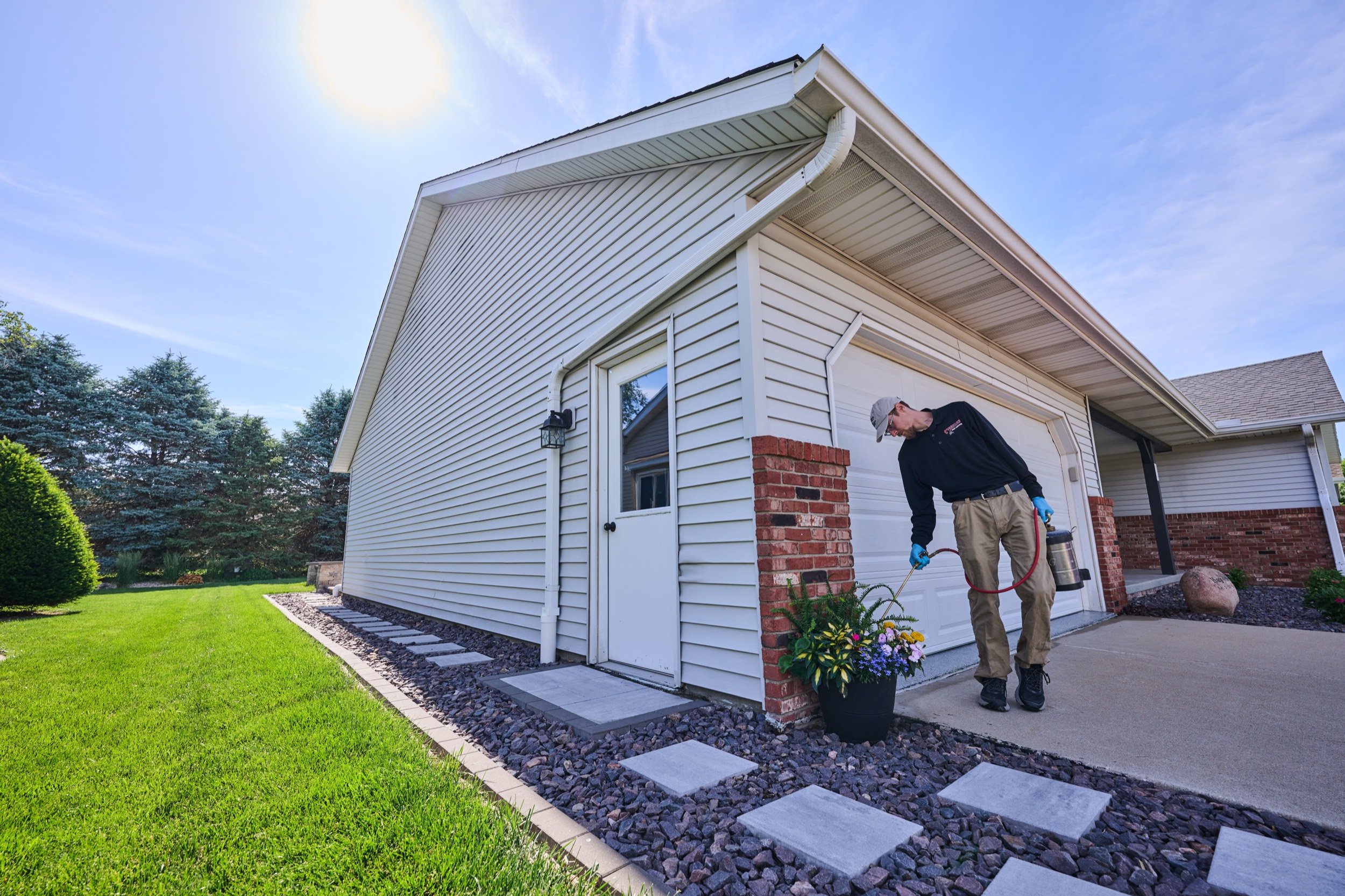 A Markley's Pest Services technician applying an exterior perimeter treatment along the foundation and garage of a Central Illinois home.